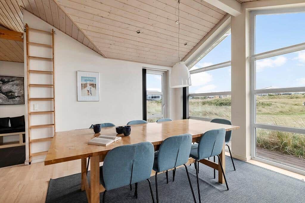 Esszimmer mit Holztisch, blauen Stühlen und großem Fensterblick auf die Landschaft.