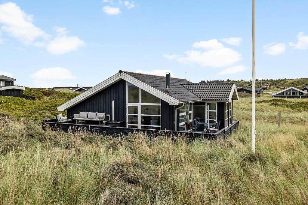 Moderne Holzhütte mit Terrasse und großem Fenster im Grasland.