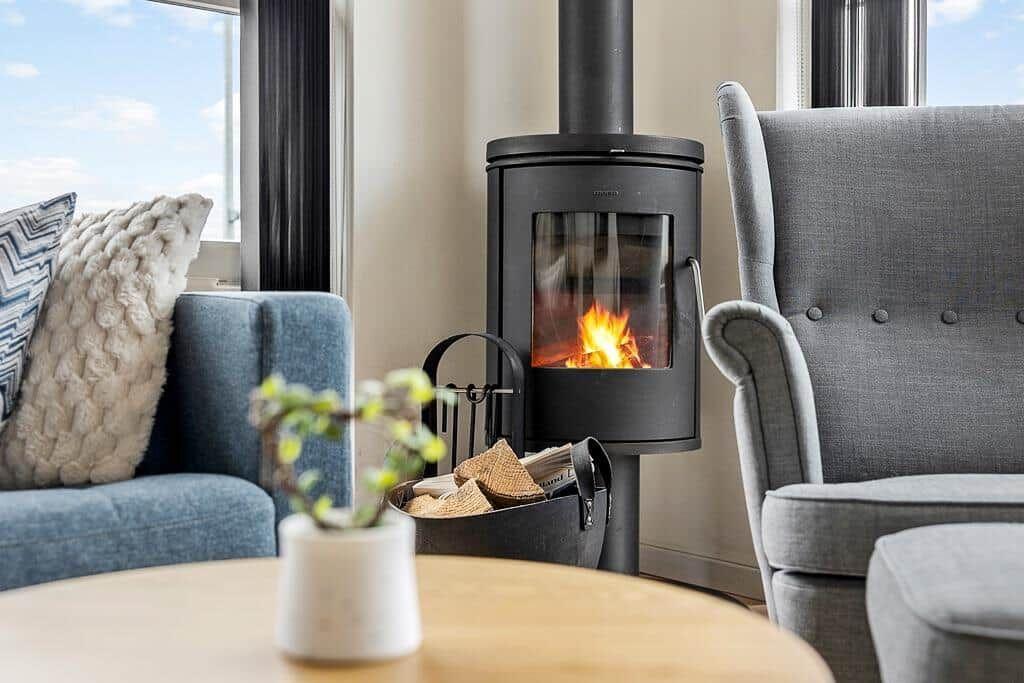 Ein Kaminofen mit brennendem Feuer zwischen einem blauen und grauen Sessel.