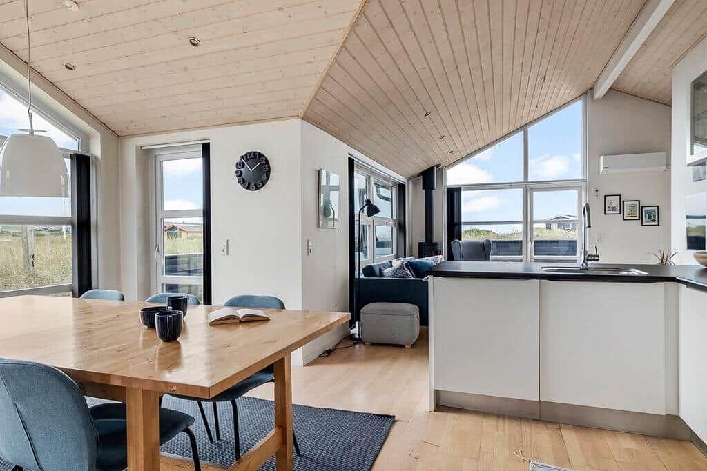 Moderne Küche mit Essbereich und großzügigen Fenstern. Holzdecke und helles Interieur.