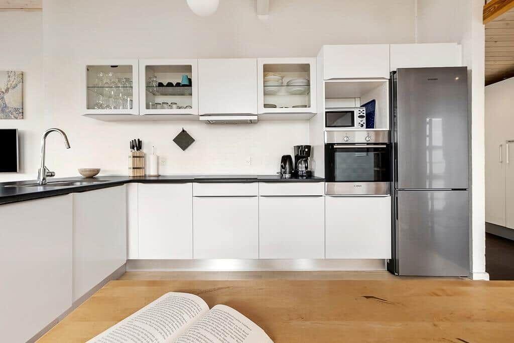 Moderne Küche mit weißen Schränken, Edelstahlgeräten und Holzboden.