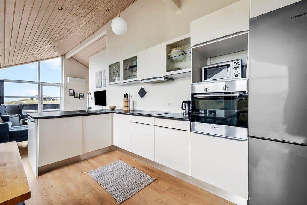 Moderne Küche mit weißen Schränken, Edelstahlgeräten und Holzboden.