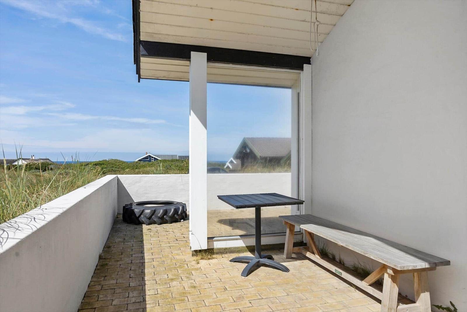 Terrasse mit Tisch, Bank und Aussicht auf Strand und Grünland.