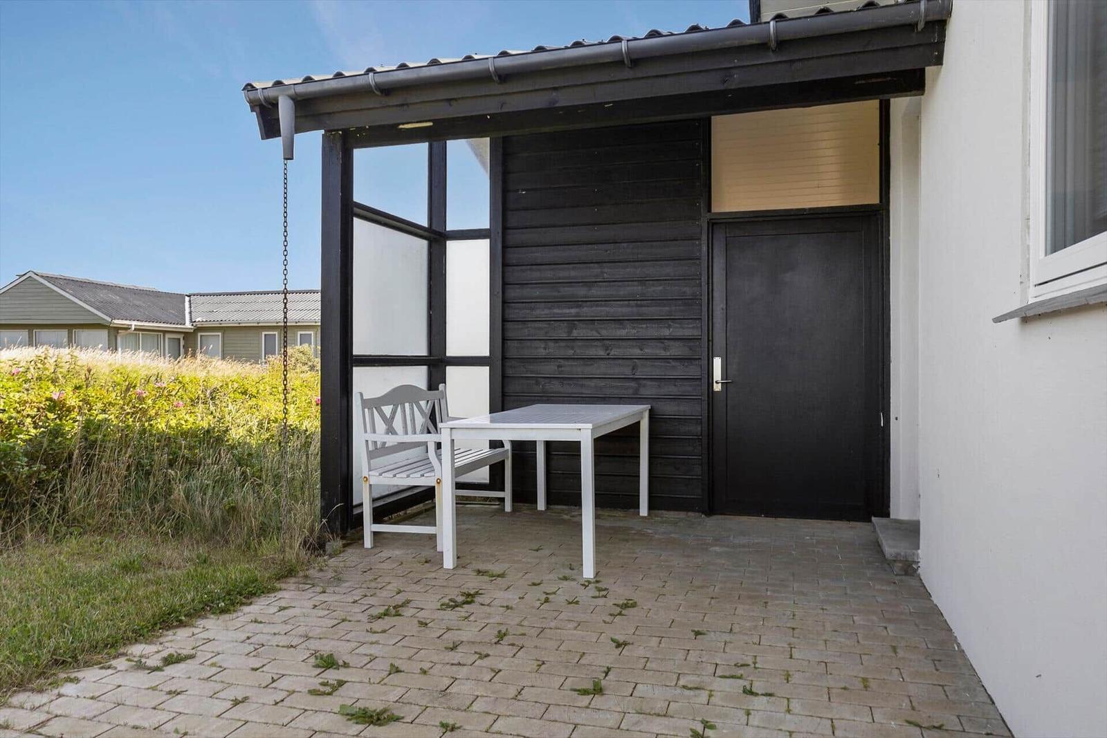 Terrasse mit Tisch und Stuhl unter Vordach. Hintergrund: Grünfläche und Gebäude.