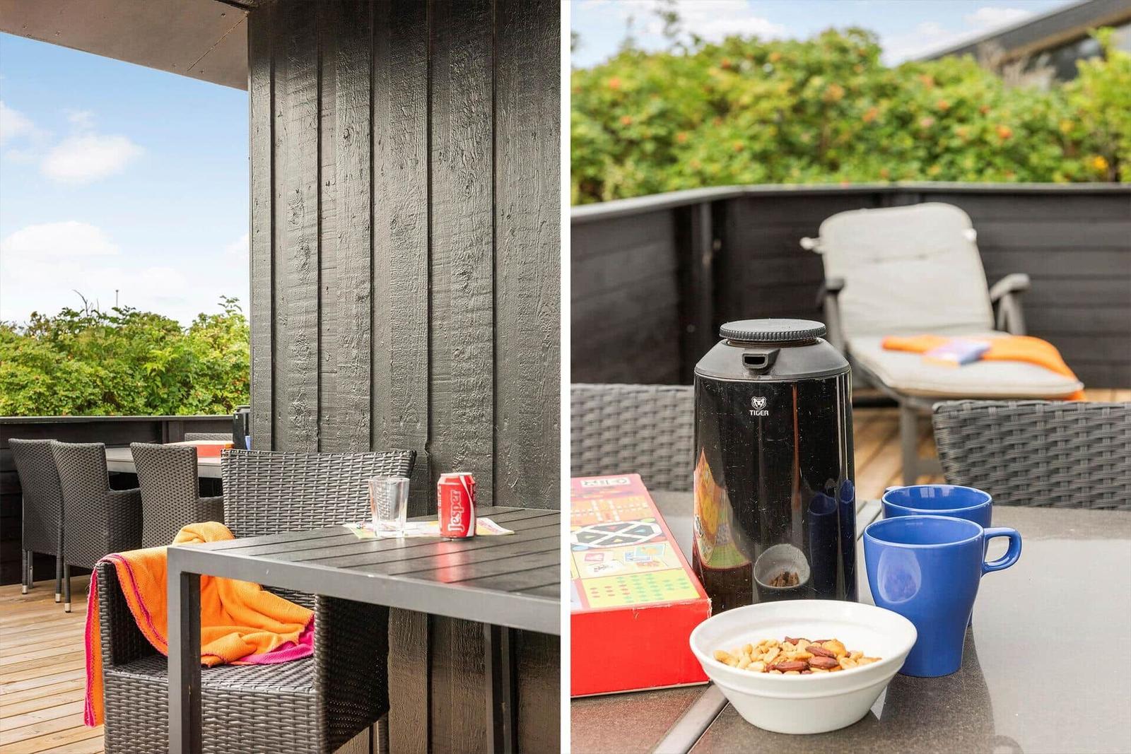 Terrasse mit Tisch, Stühlen und Blick auf Grünflächen. Auf dem Tisch stehen Tassen, eine Schale und ein Kaffeekocher.