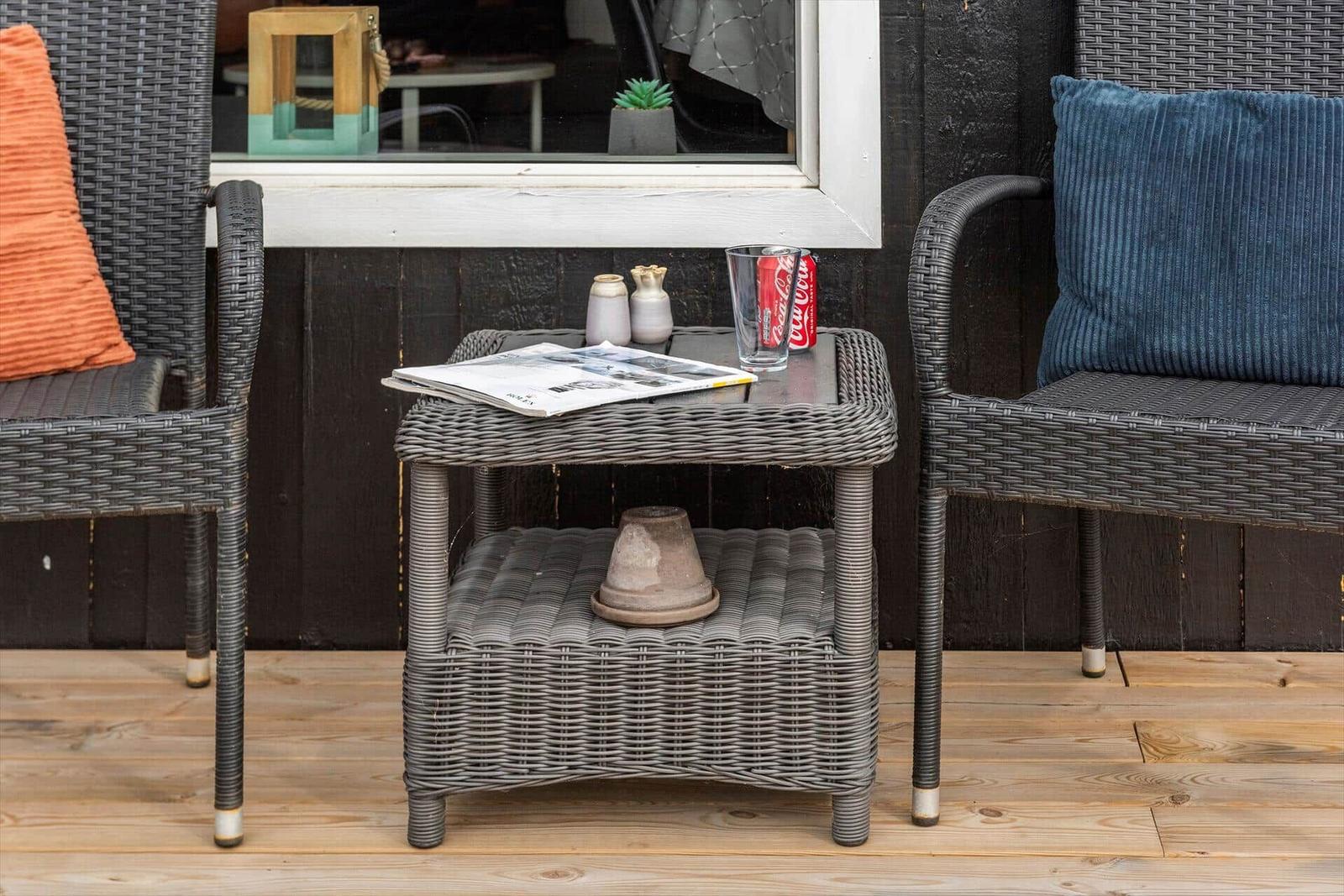 Außentisch mit Zeitschrift, Getränk und Dekoration zwischen zwei Stühlen auf Terrasse.