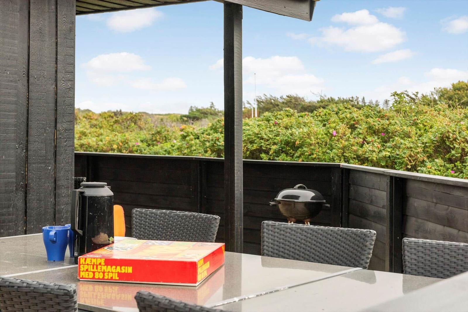Terrasse mit Tisch, Stühlen, Grill und Blick auf grüne Landschaft.