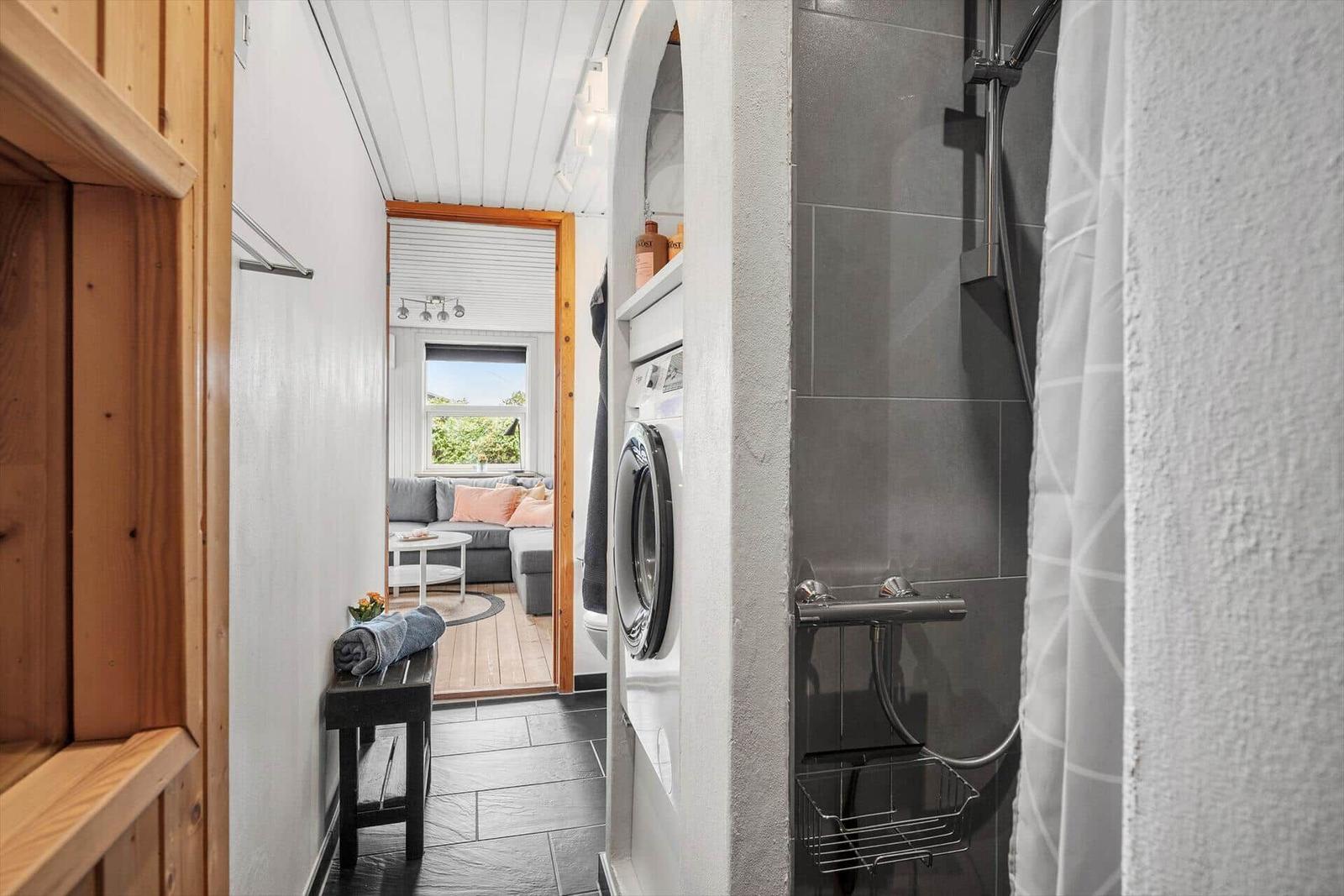 Flur mit Waschmaschine und Dusche, Blick in Wohnbereich mit Sofa und Fenster.