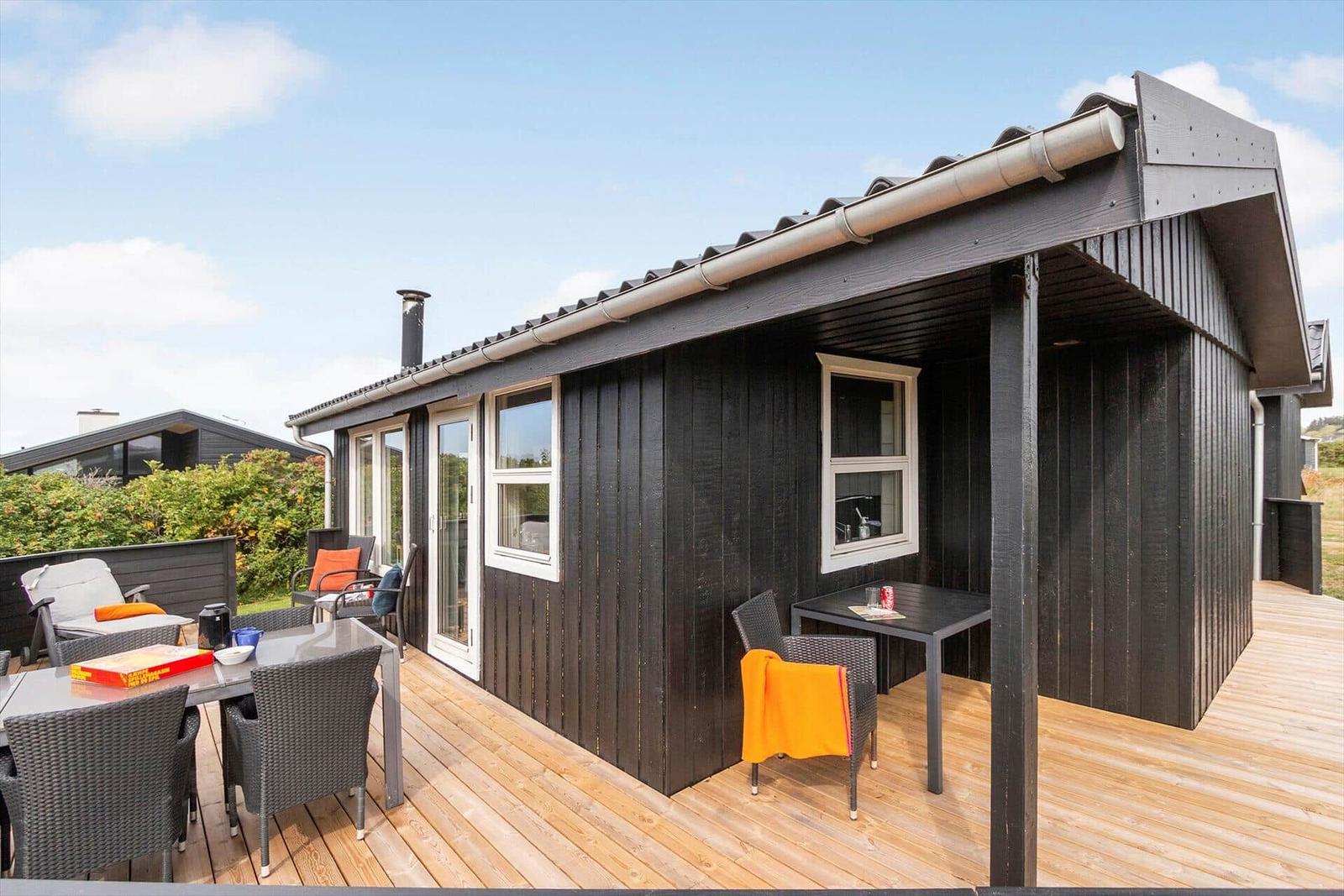 Schwarzes Holzhaus mit Terrasse und Gartenmöbeln unter blauem Himmel.