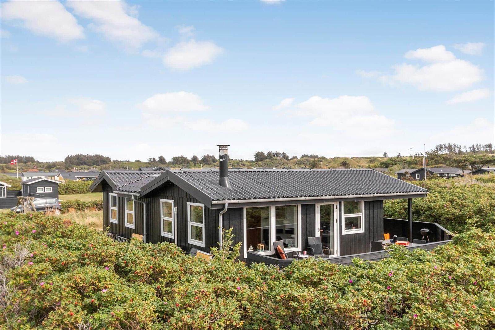 Moderne Holzhütte mit Terrasse und Grillplatz. Umgeben von Grünflächen und Blick auf die Landschaft.