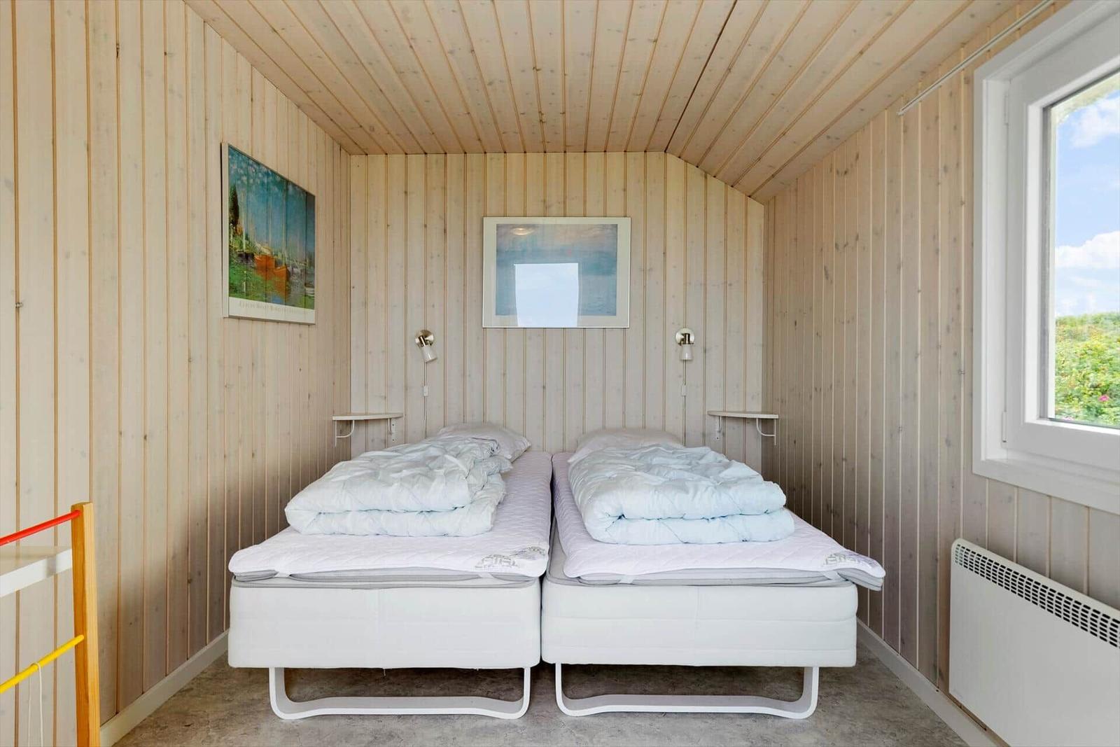 Zwei Betten mit weißen Matratzen und Bettwäsche in einem holzverkleideten Raum mit Fenster.