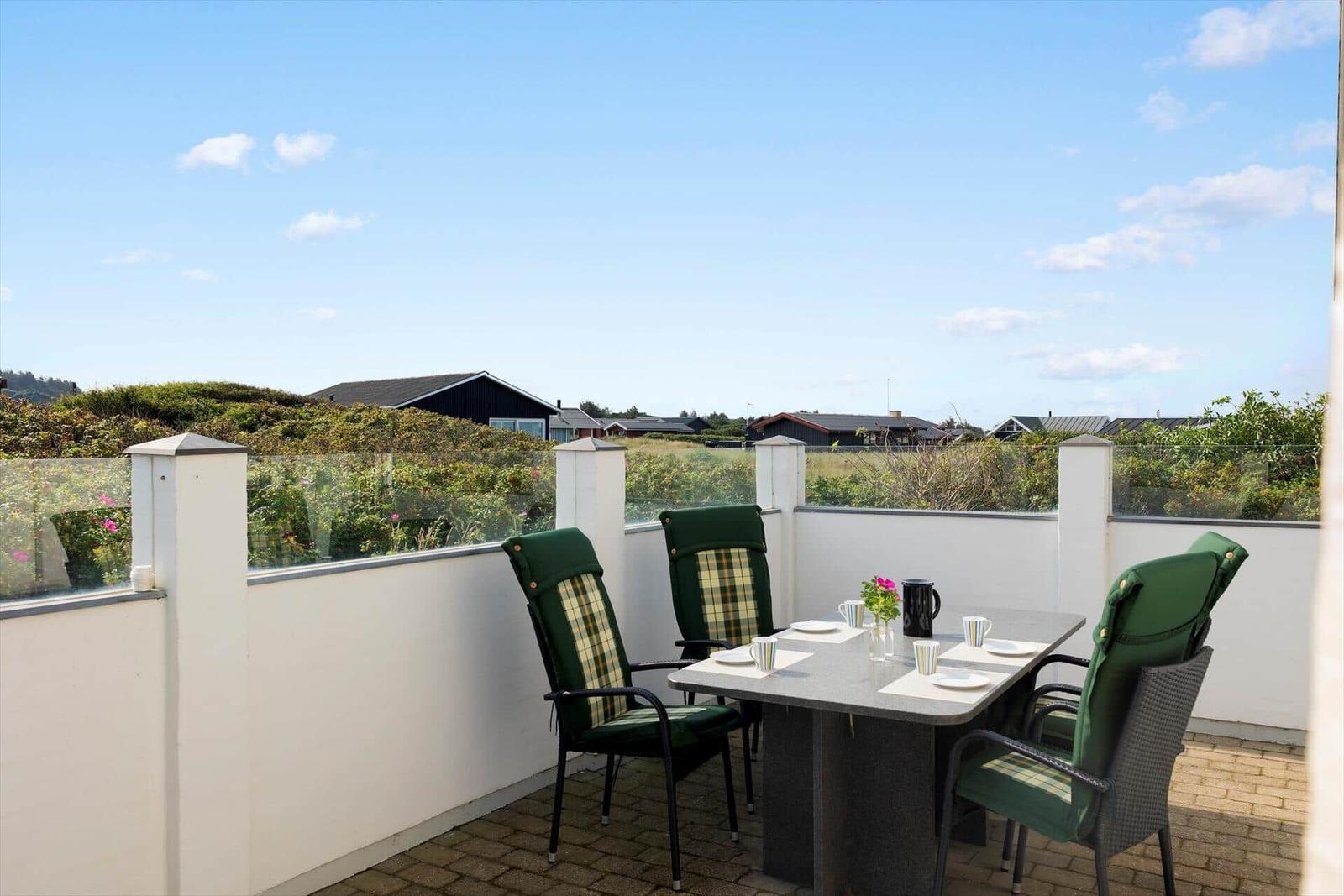 Terrasse mit Tisch und vier grünen Stühlen. Blick auf Grünflächen und Häuser.
