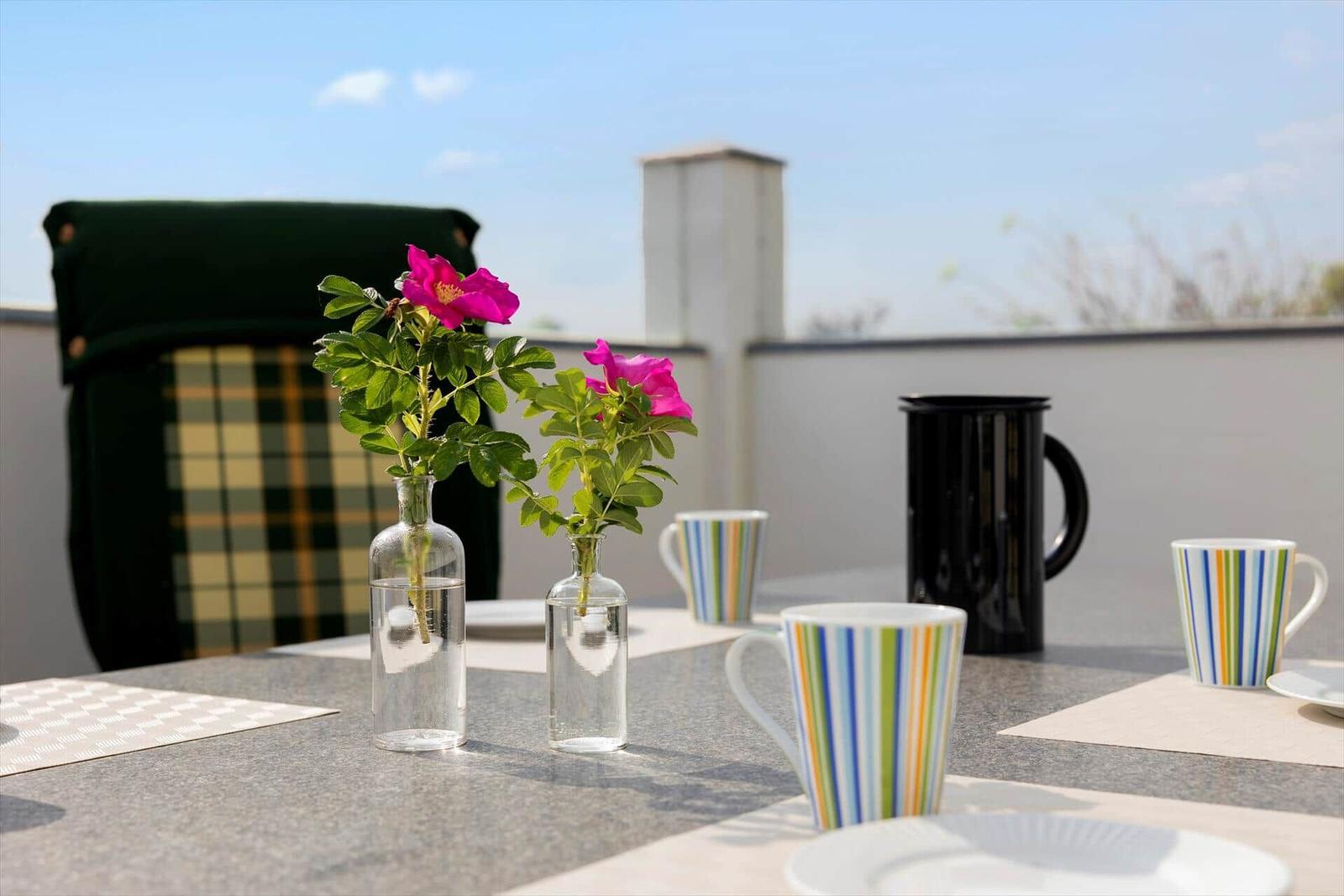 Tisch auf Balkon mit Blumen in Gläsern und Tassen.