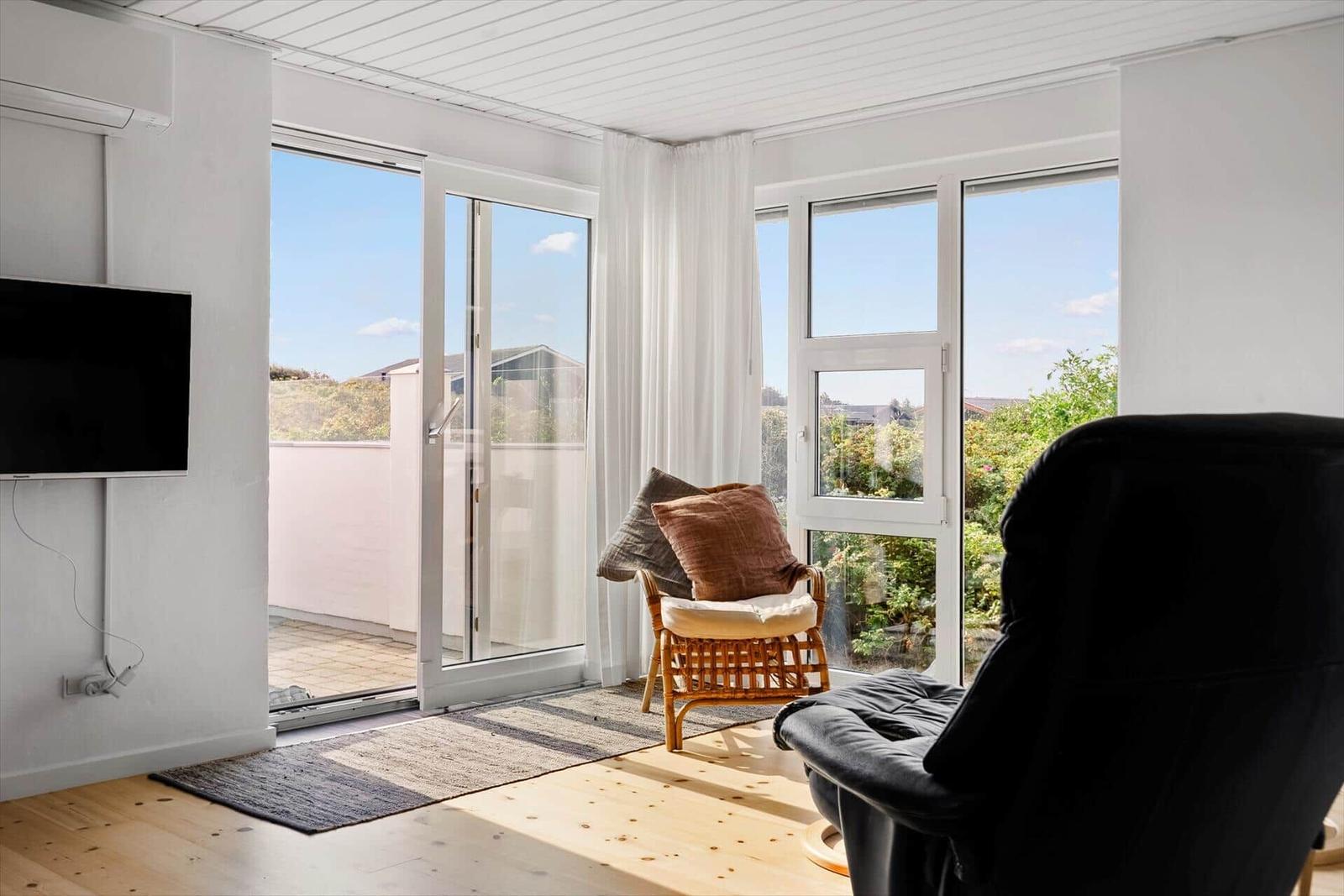Wohnraum mit TV, Schiebetür und Sitzgelegenheiten. Blick auf Balkon und Garten.