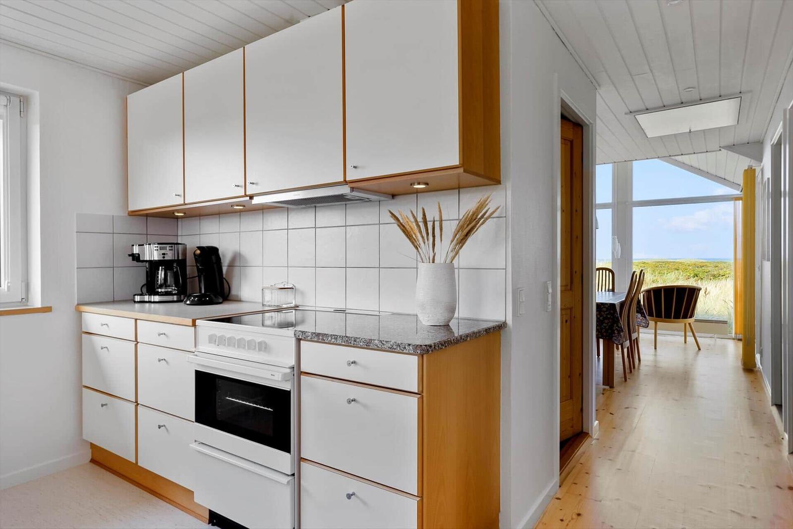 Küche mit weißen Schränken, Steinplatte und Blick in Esszimmer mit Blick auf Grasland.