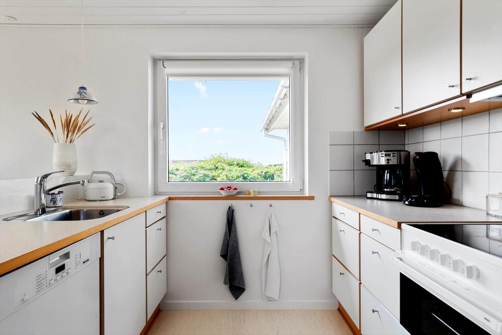 Küche mit Fenster, Spüle, Kochfeld und Küchengeräten.