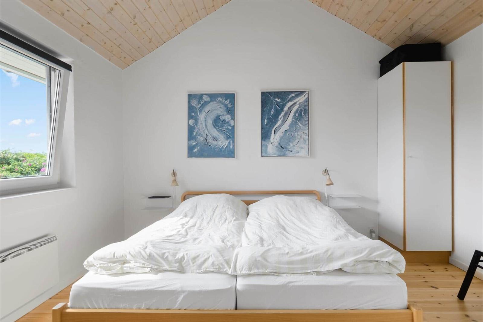 Schlafzimmer mit Doppelbett, Holzdecke und Fensterblick auf Grün