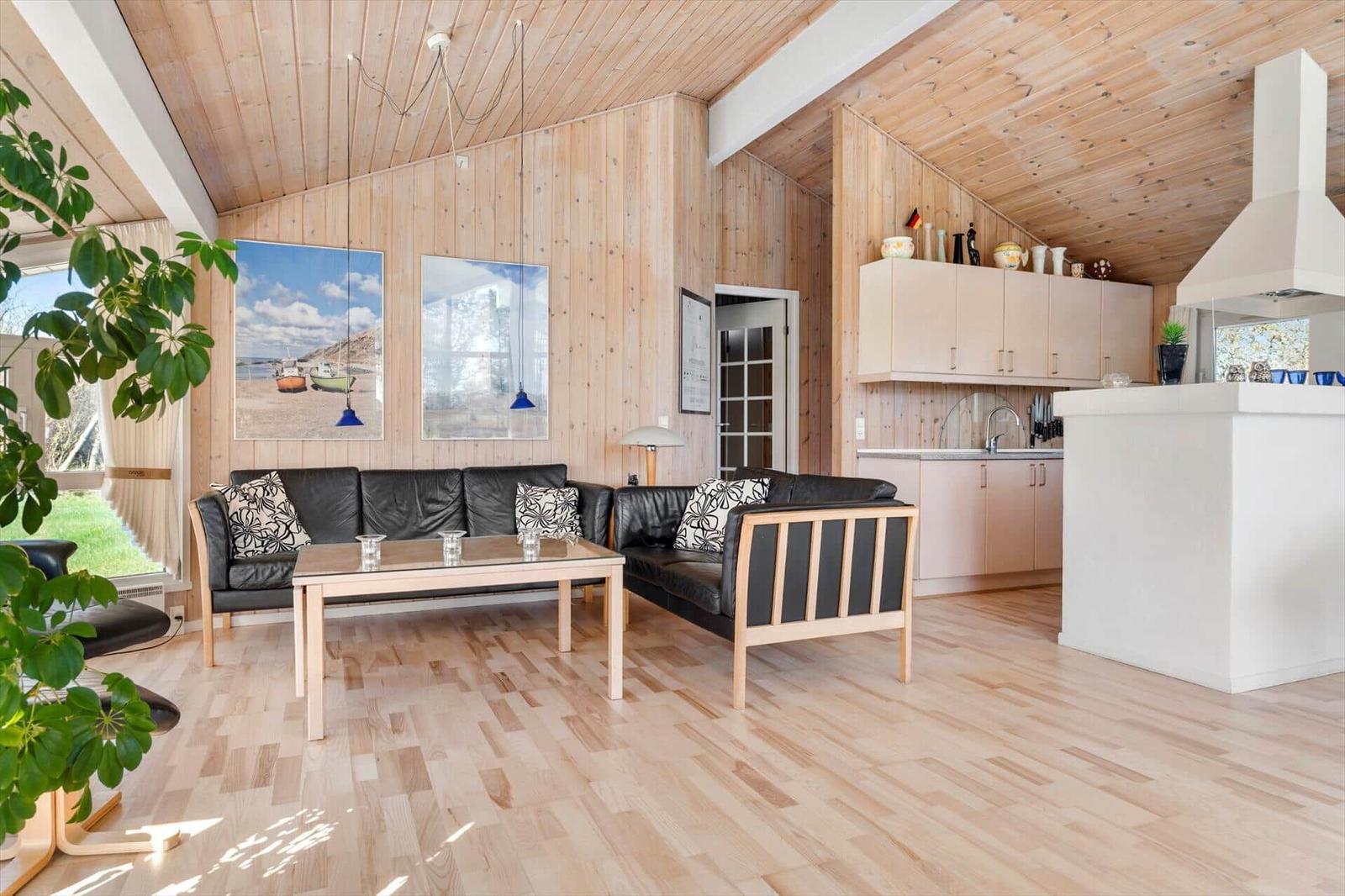 Wohnbereich mit Sofa, Tisch und Küche unter Holzdecke.