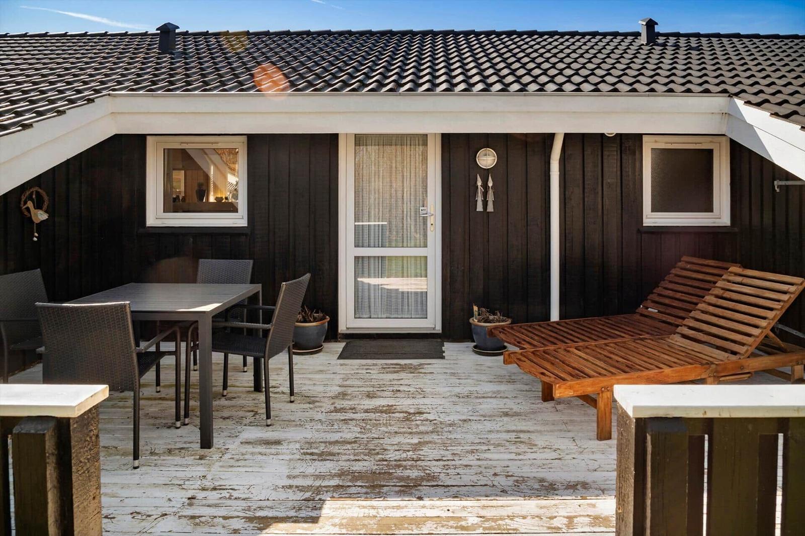 Terrasse mit Tisch, Stühlen und Liegen vor einem Haus mit dunkler Holzfassade.