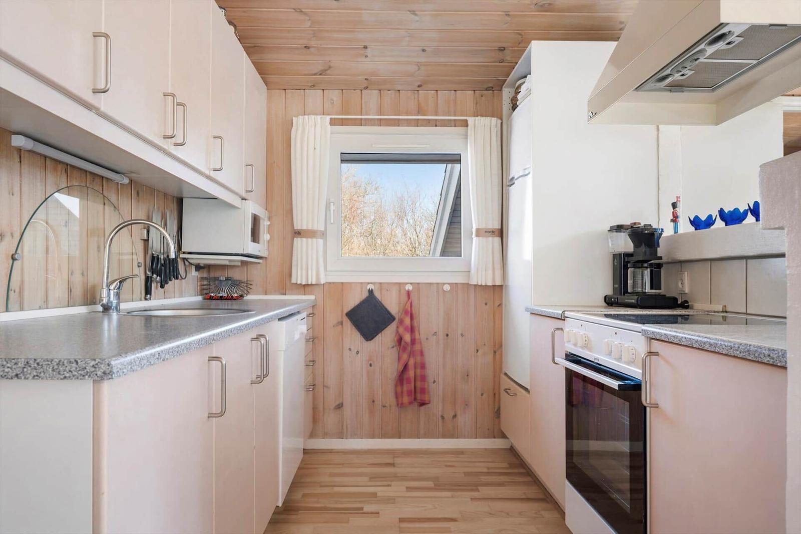 Küche mit Holzwand, Fenster, Spüle, Kühlschrank und Herd.