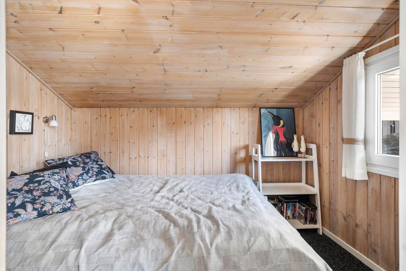 Schlafzimmer mit Holzwand und -decke, Bett mit Kissen, Bild und Regal.