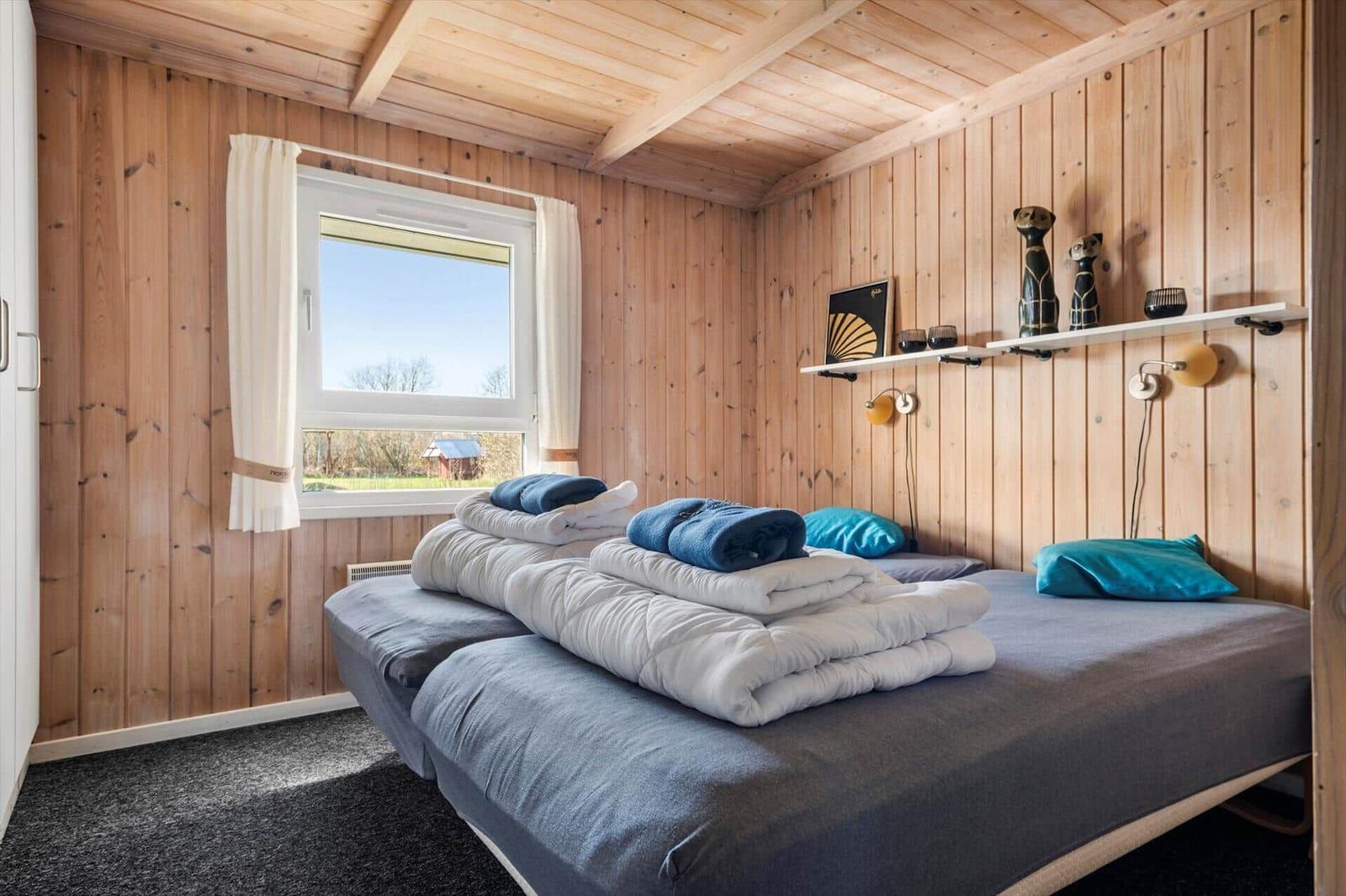 Zimmer mit Holzwänden, Bett mit Bettwäsche und Fenster mit Blick.