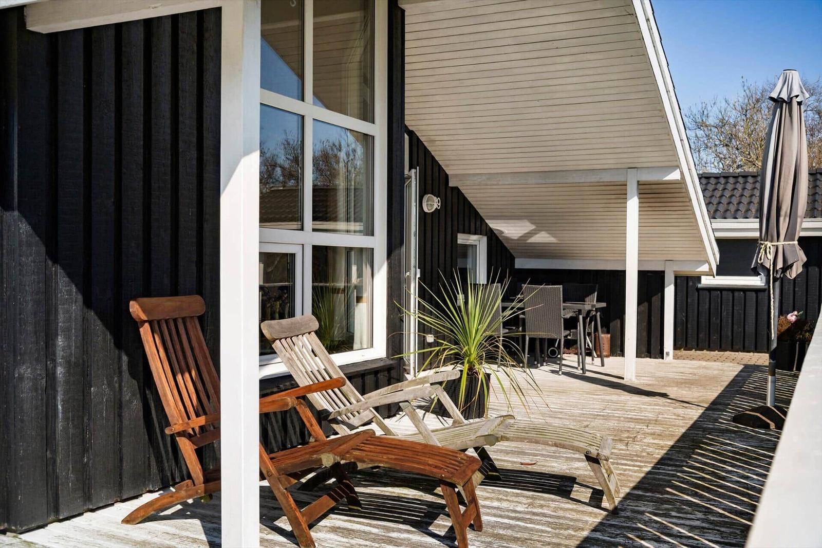 Terrasse mit Holzstühlen, Sonnenschutz und Pflanze vor einem Haus mit schwarzer Fassade.