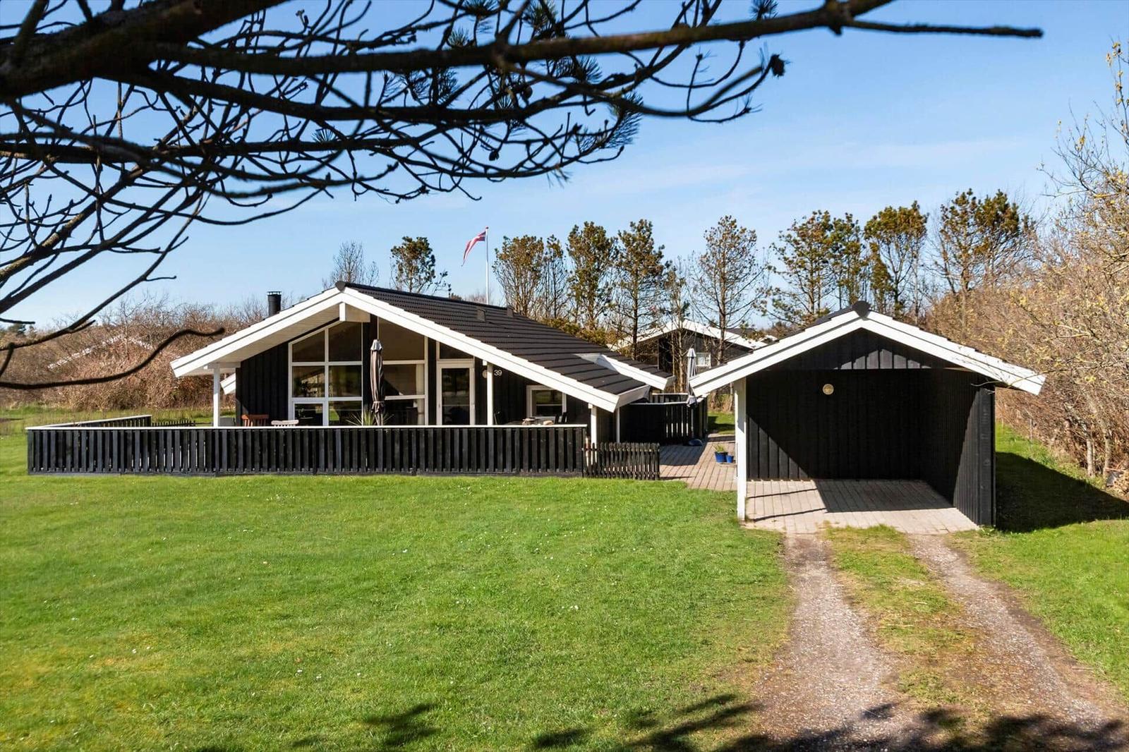 Schwarze Holzhütte mit Terrasse und Carport auf grünem Grundstück.