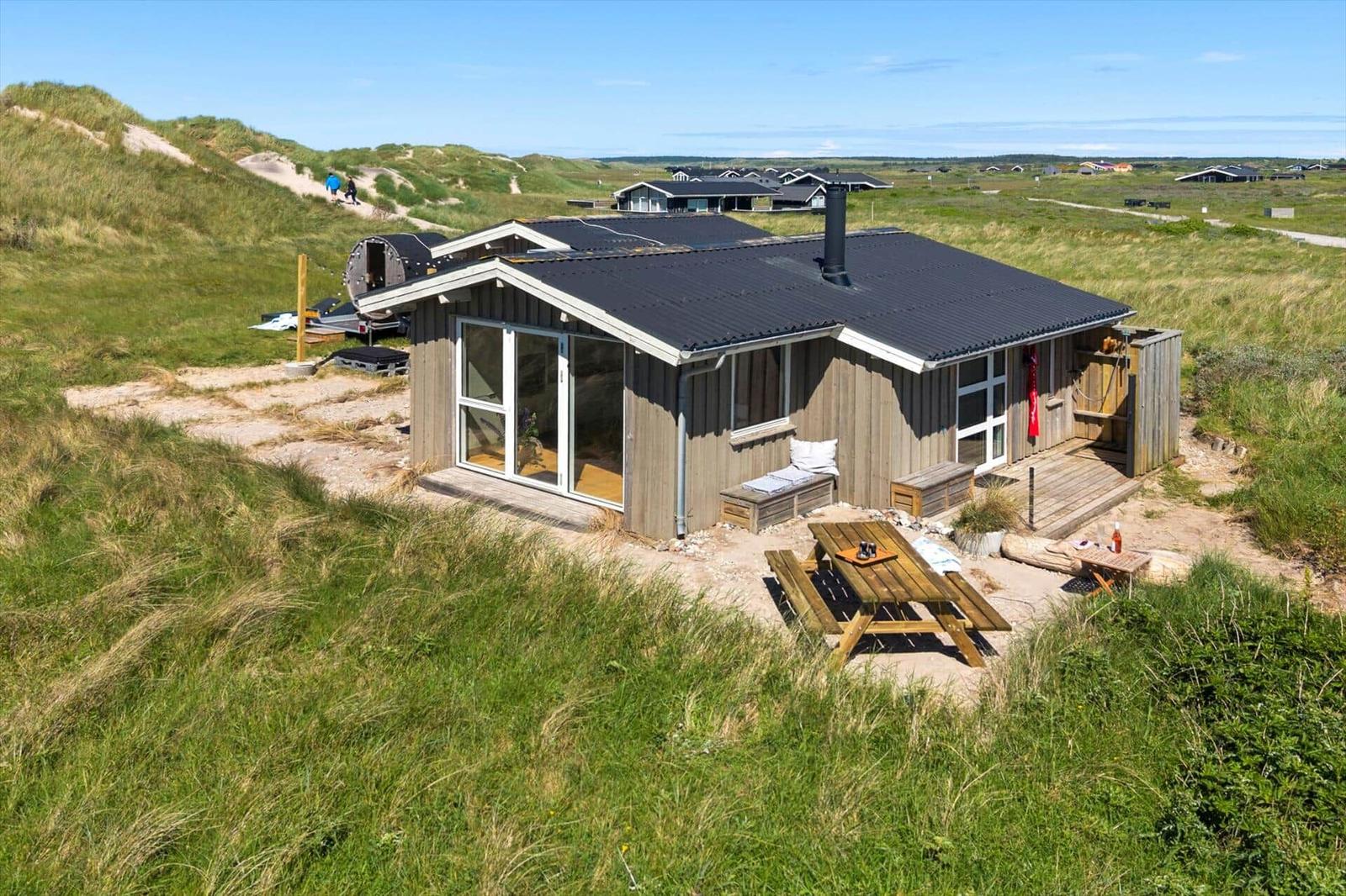 Holzhütte mit Terrasse und Grillplatz in grüner Landschaft.