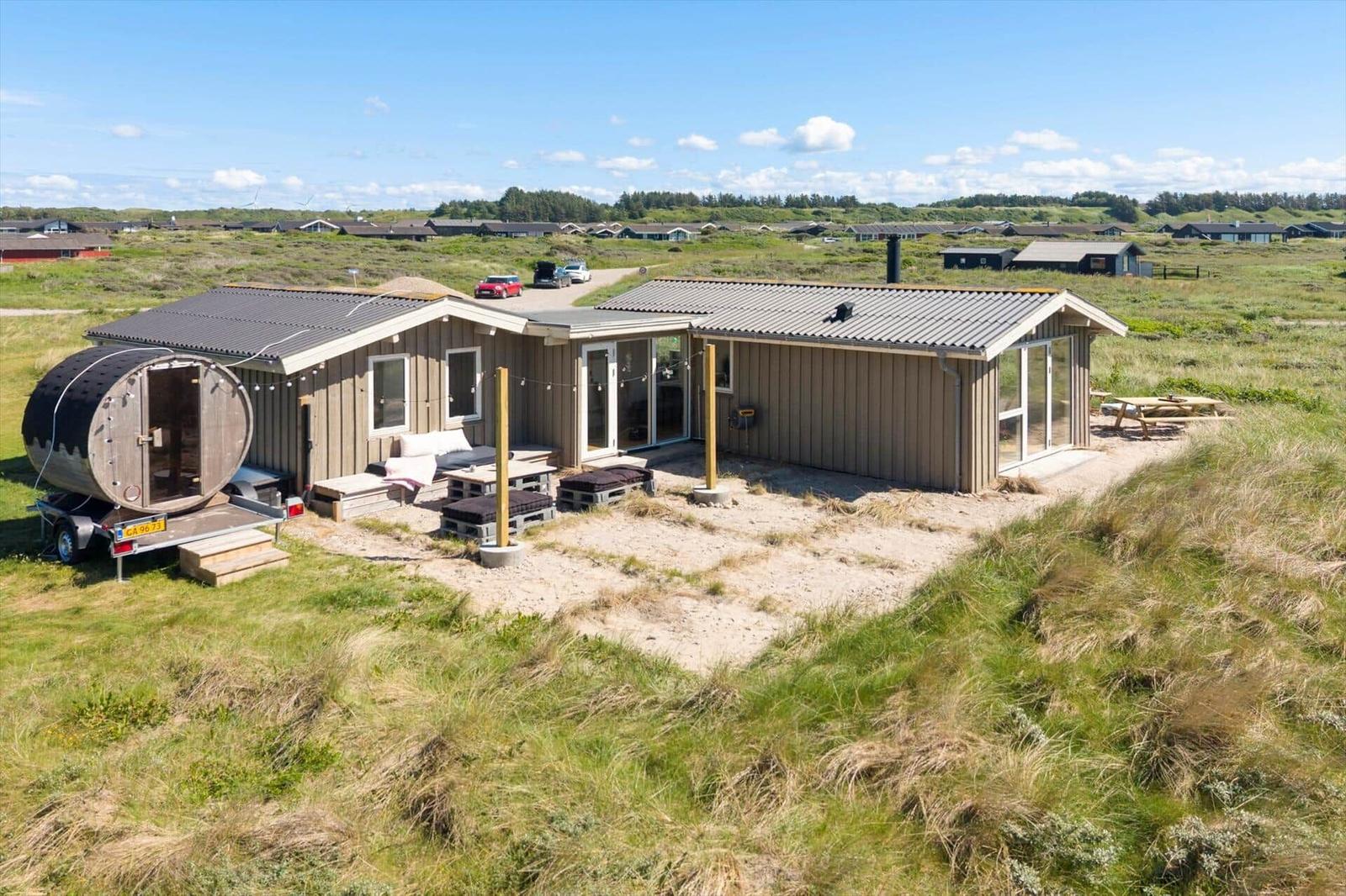 Moderne Holzhütte mit Sauna und Terrasse in grüner Landschaft.