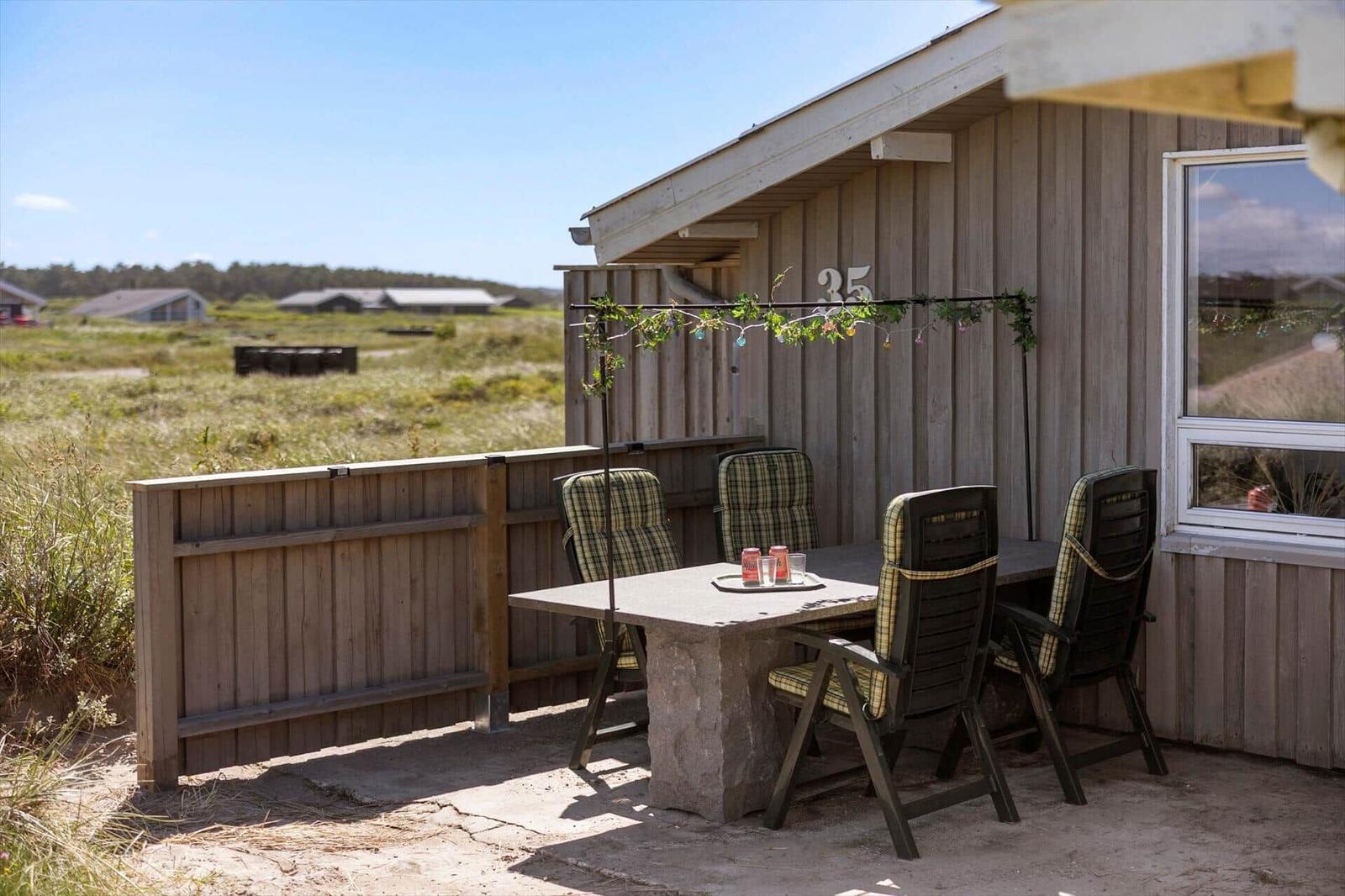 Terrasse mit Tisch und Stühlen vor einem Holzhaus mit Fenster und Zaun.