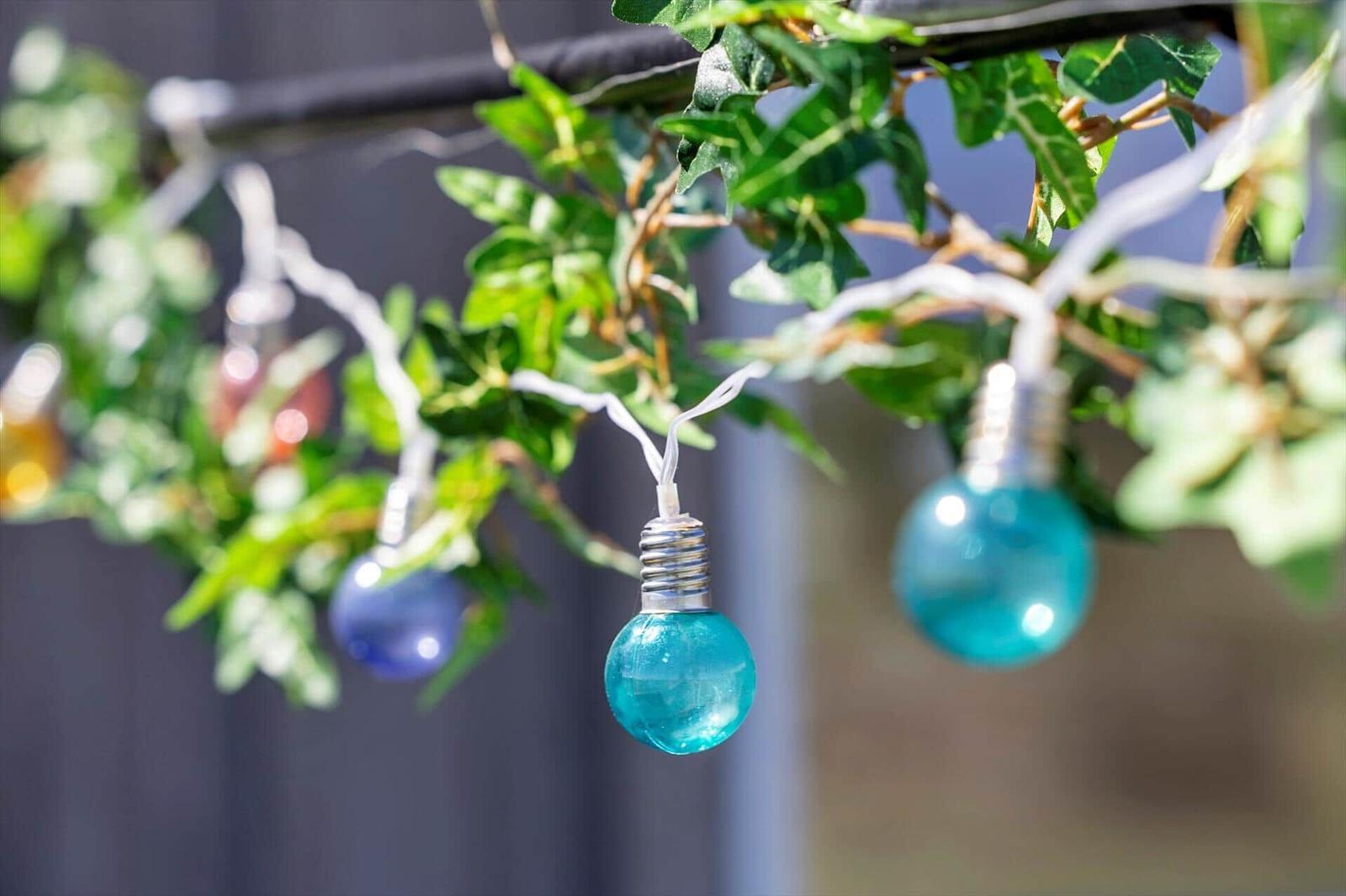 Blaue Glühbirnenlichterkette hängt an grünen Blättern im Freien.