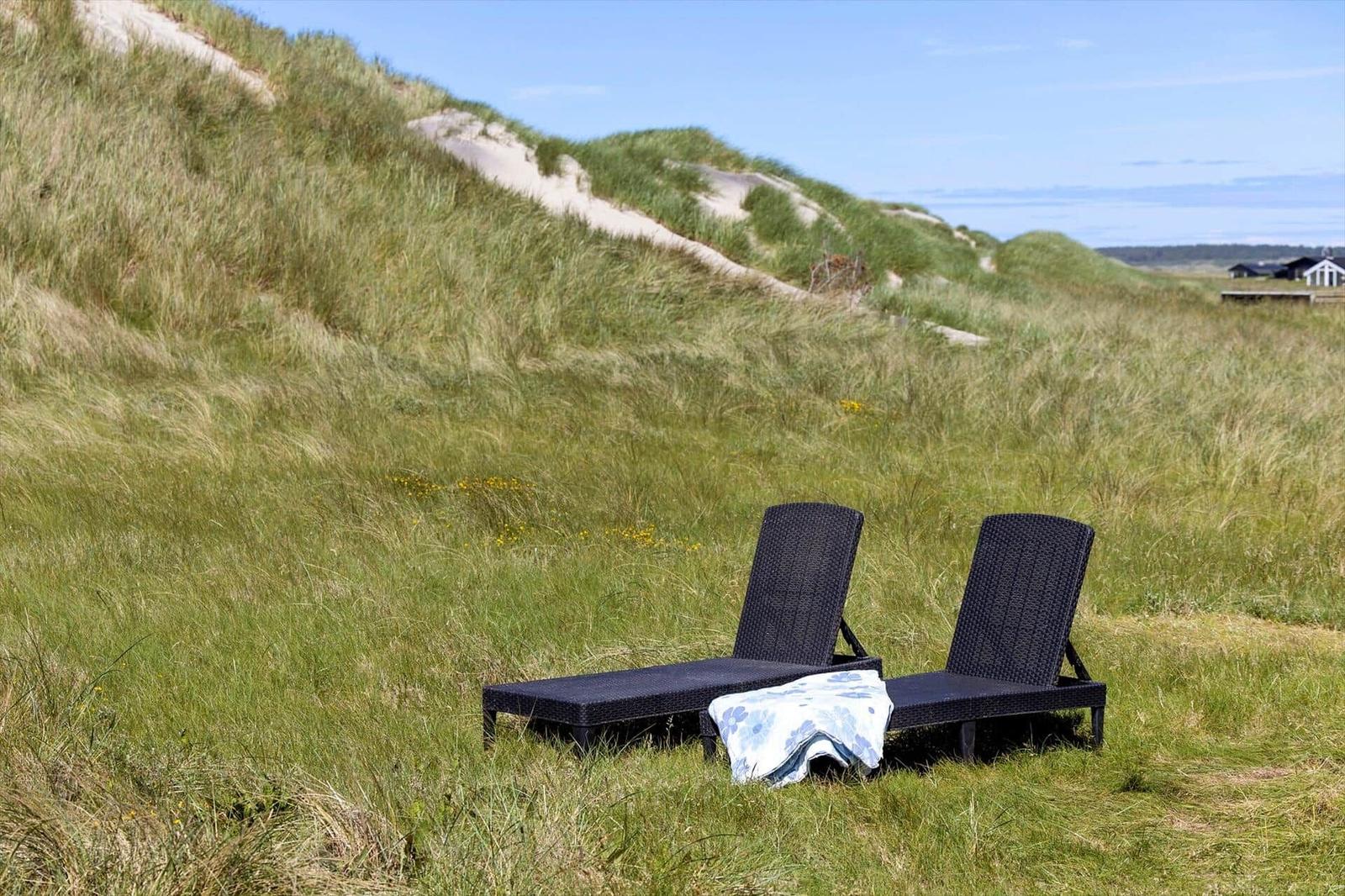 Zwei Liegestühle stehen auf einer grasbewachsenen Düne. Ein Handtuch liegt darauf.