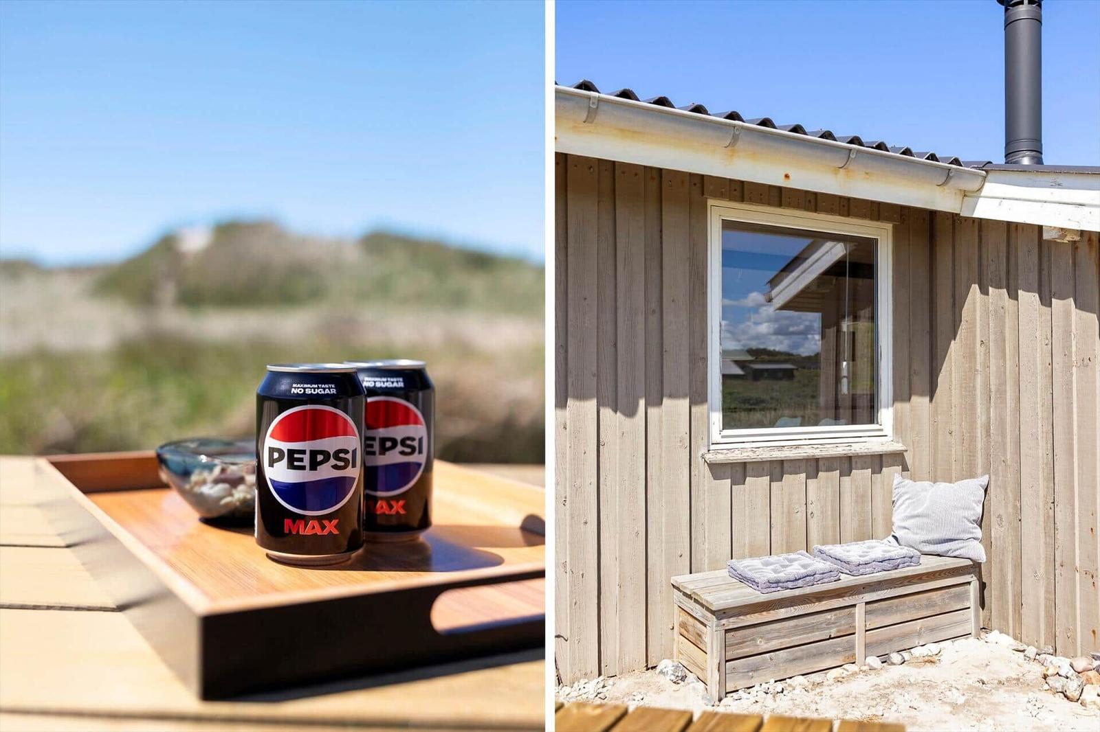 Zwei Pepsi Max Dosen auf einem Holztisch. Holzbank vor einem Haus mit Fenster.