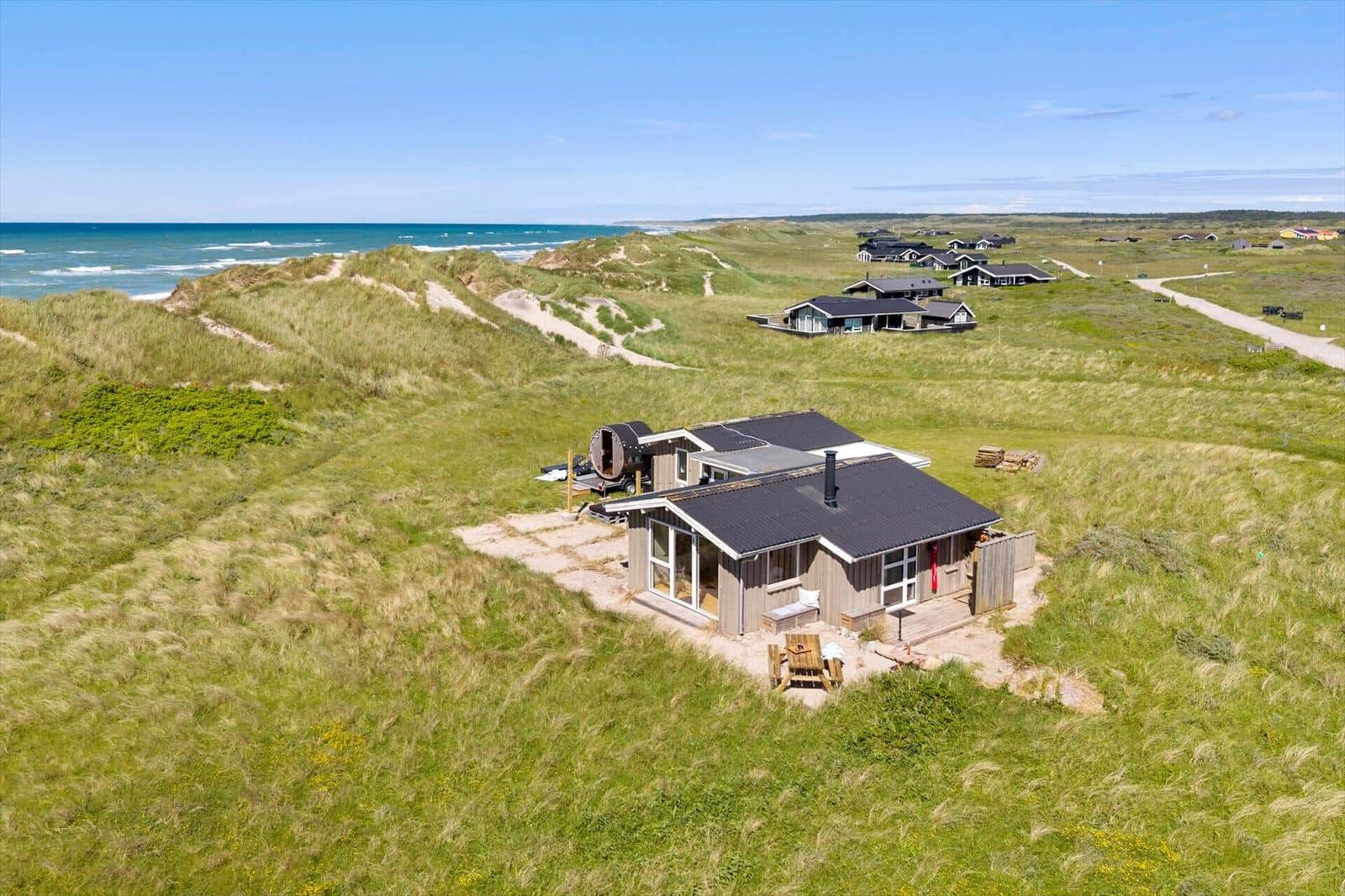 Holzhütte mit Terrasse auf Dünen, Blick auf das Meer.