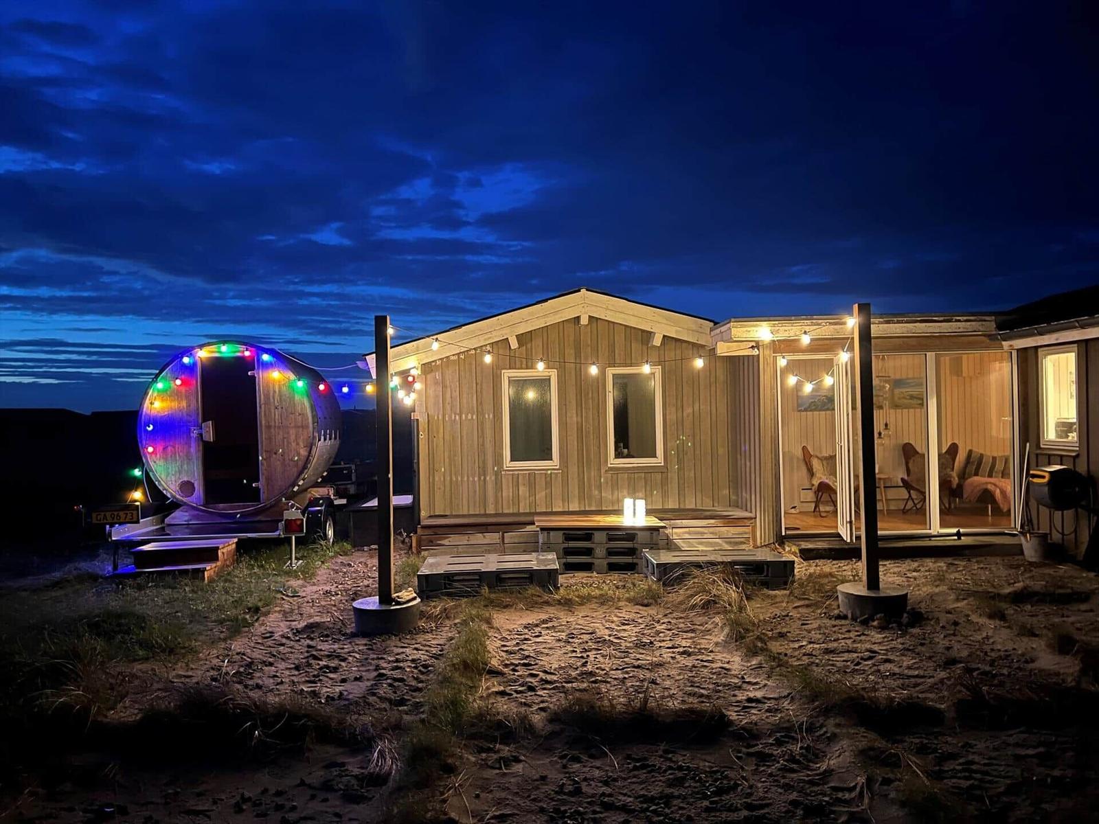 Hütte mit Lichterkette und runden Saunabereich bei Nacht.