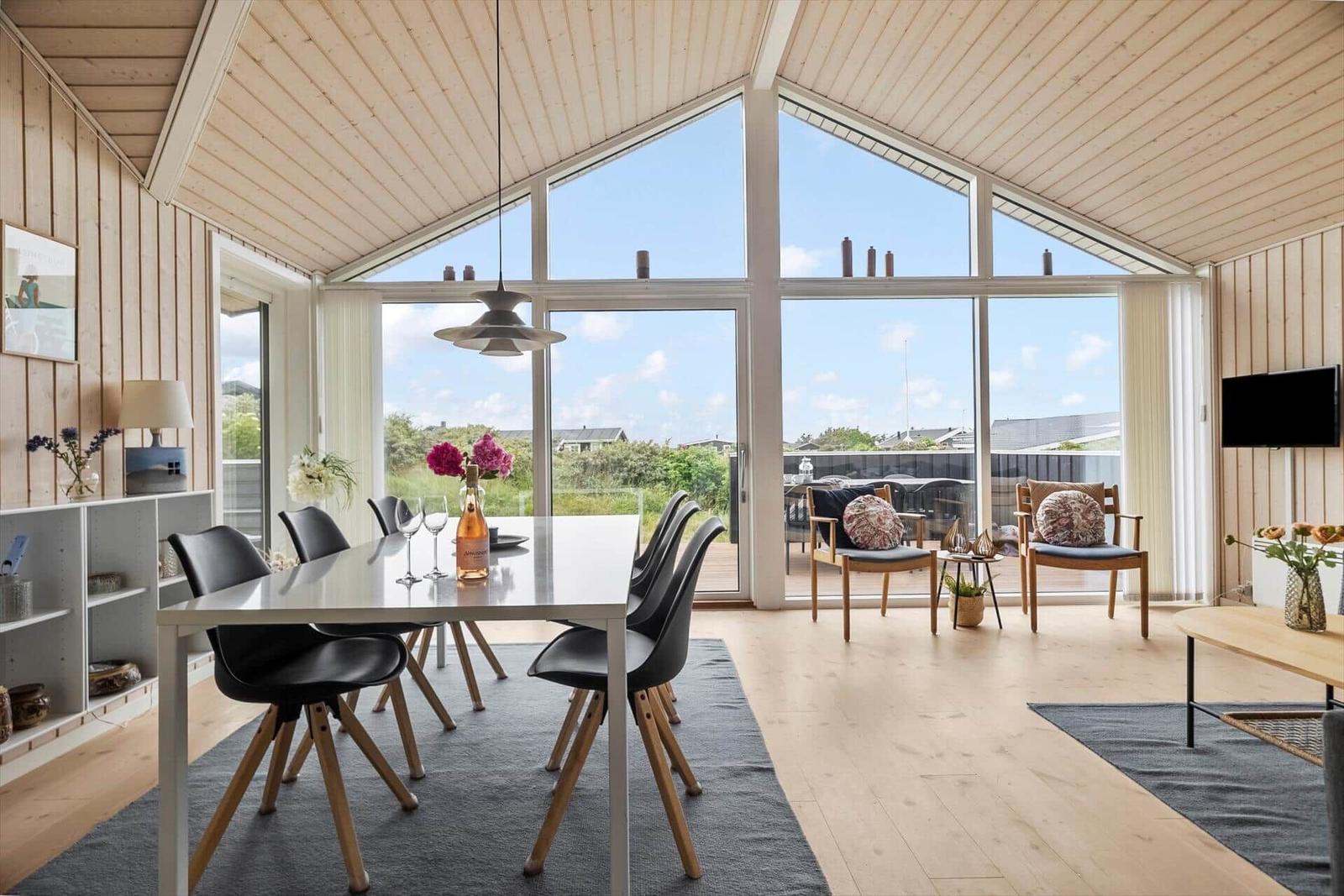 Ein Essbereich mit Tisch und Stühlen, große Fenster und eine Terrasse mit Sitzgelegenheiten.