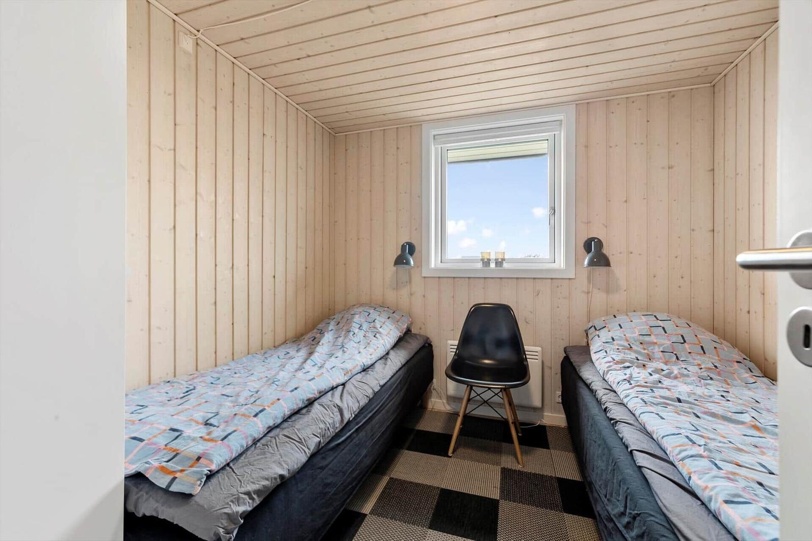 Zwei Einzelbetten, ein schwarzer Stuhl und ein Fenster in einem Holzraum.