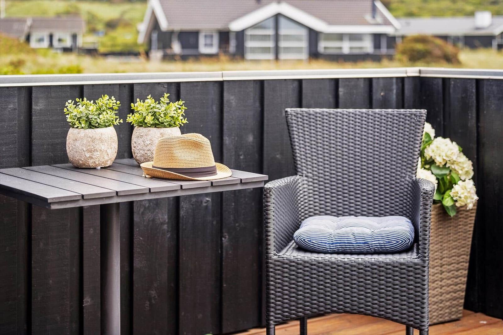 Terrasse mit Stuhl, Tisch, Pflanzen und Hut. Blick auf Ferienhaus im Hintergrund.
