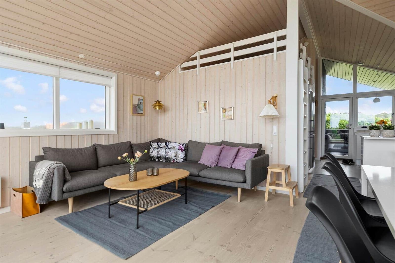 Ein Wohnzimmer mit grauem Sofa, Holztisch und Fenster. An der Wand hängen Bilder.