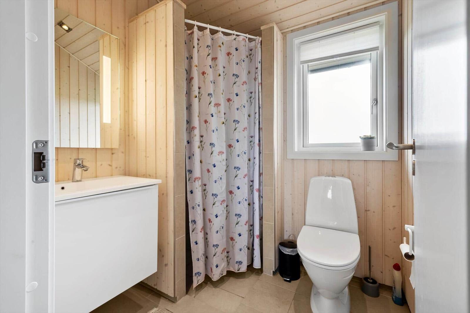 Badezimmer mit Dusche, Toilette und Waschbecken. Holzwände und Fenster.