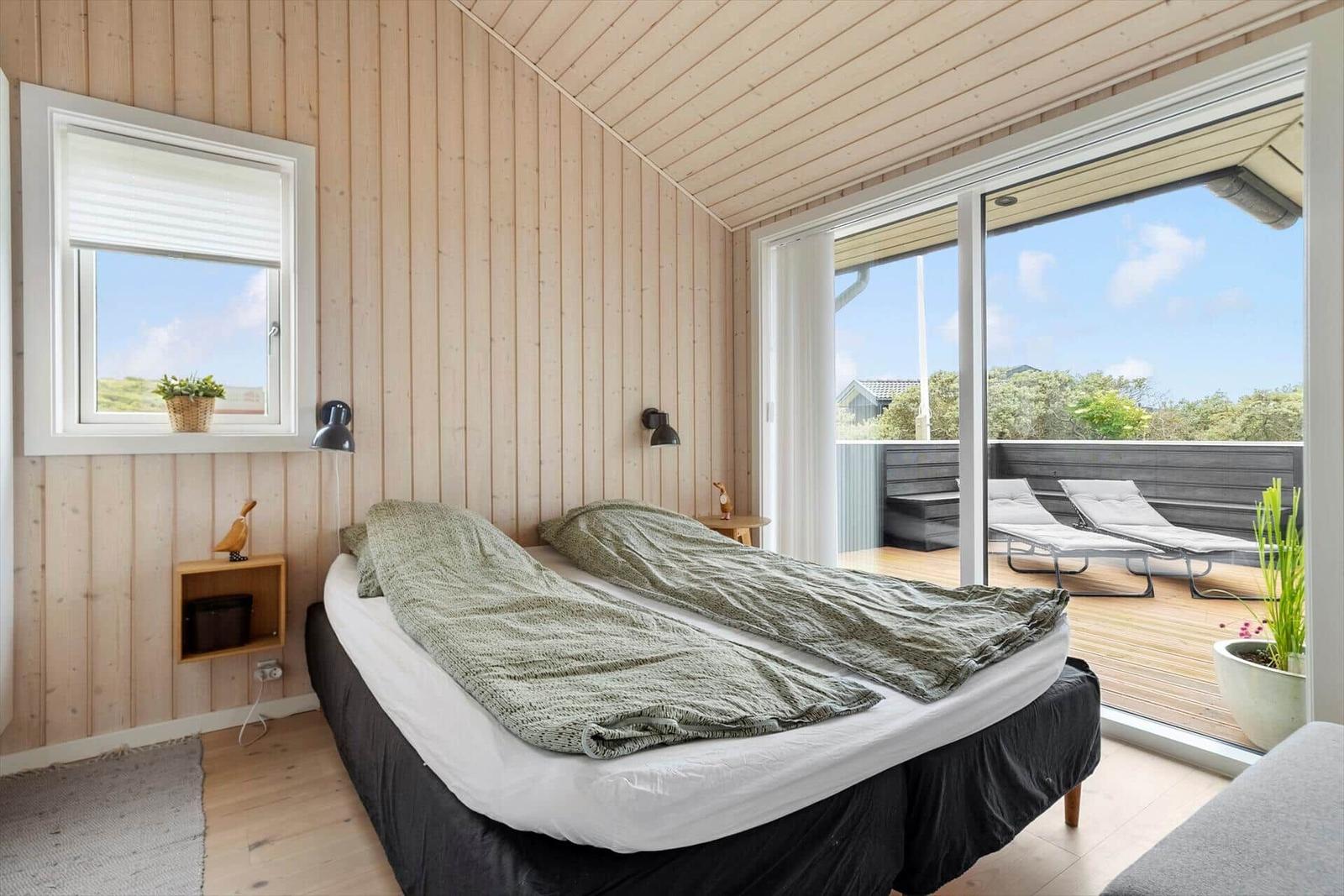 Schlafzimmer mit Balkon, Bett, Fenster und Holzwand.