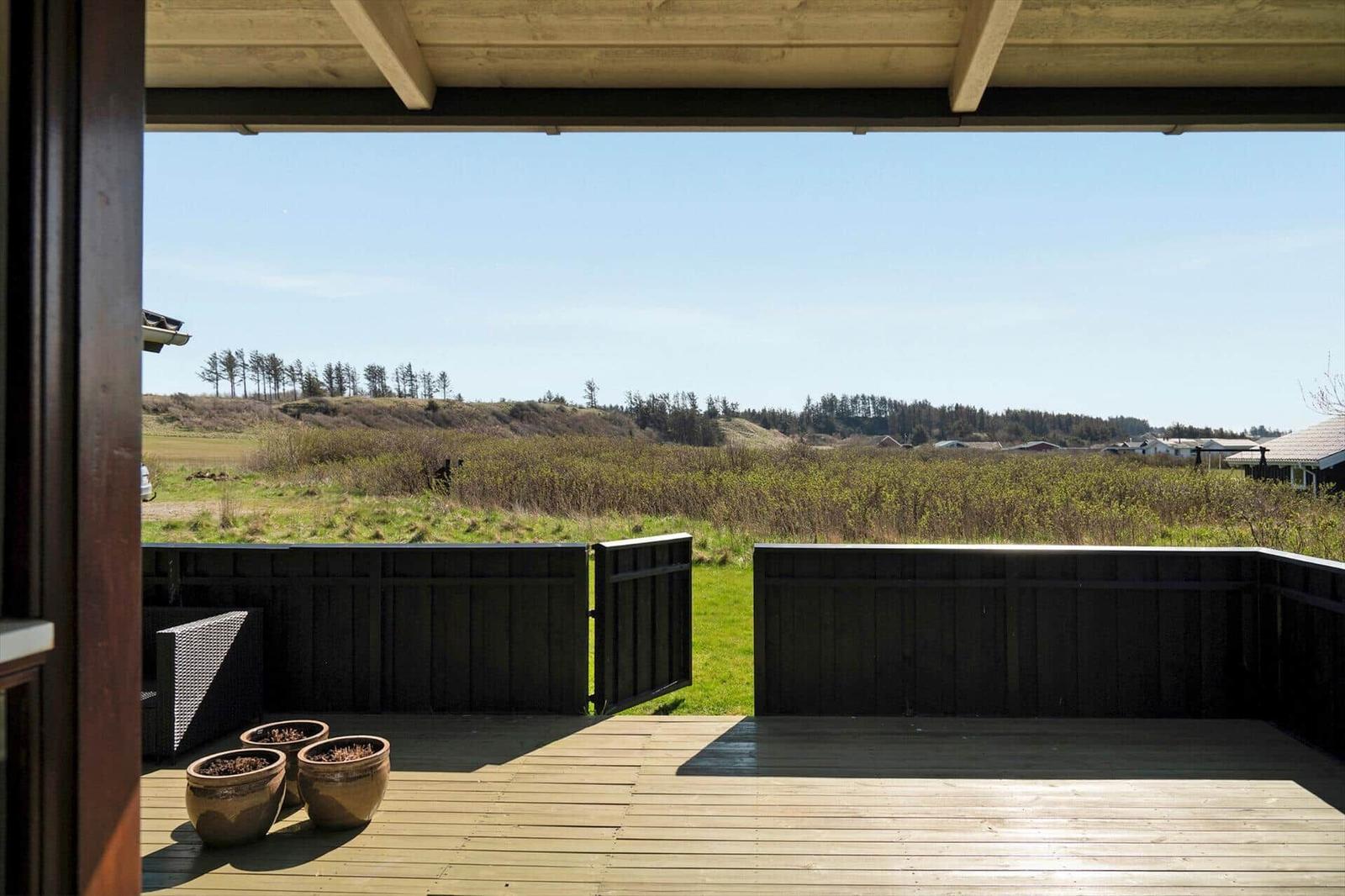 Terrasse mit Holzdecke und Blick auf grüne Wiesen und Bäume.
