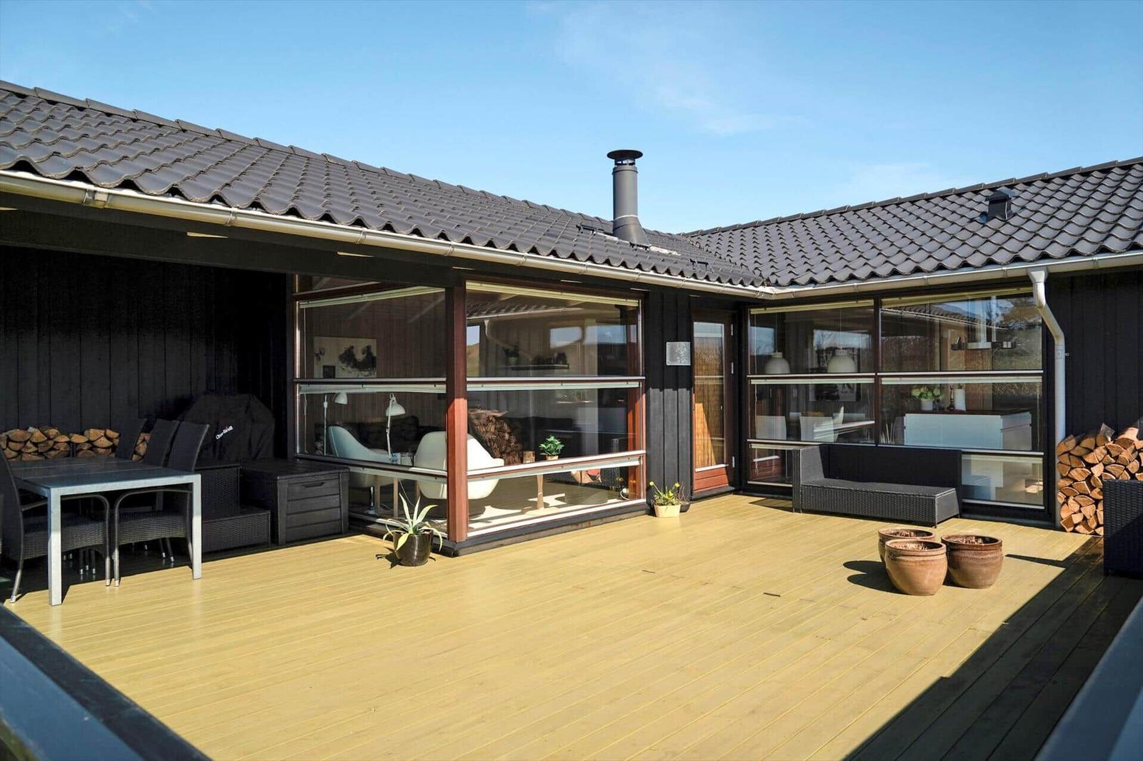 Terrasse mit Sitzgelegenheiten und Blick in das Haus. Holzdielenboden und große Fenster.