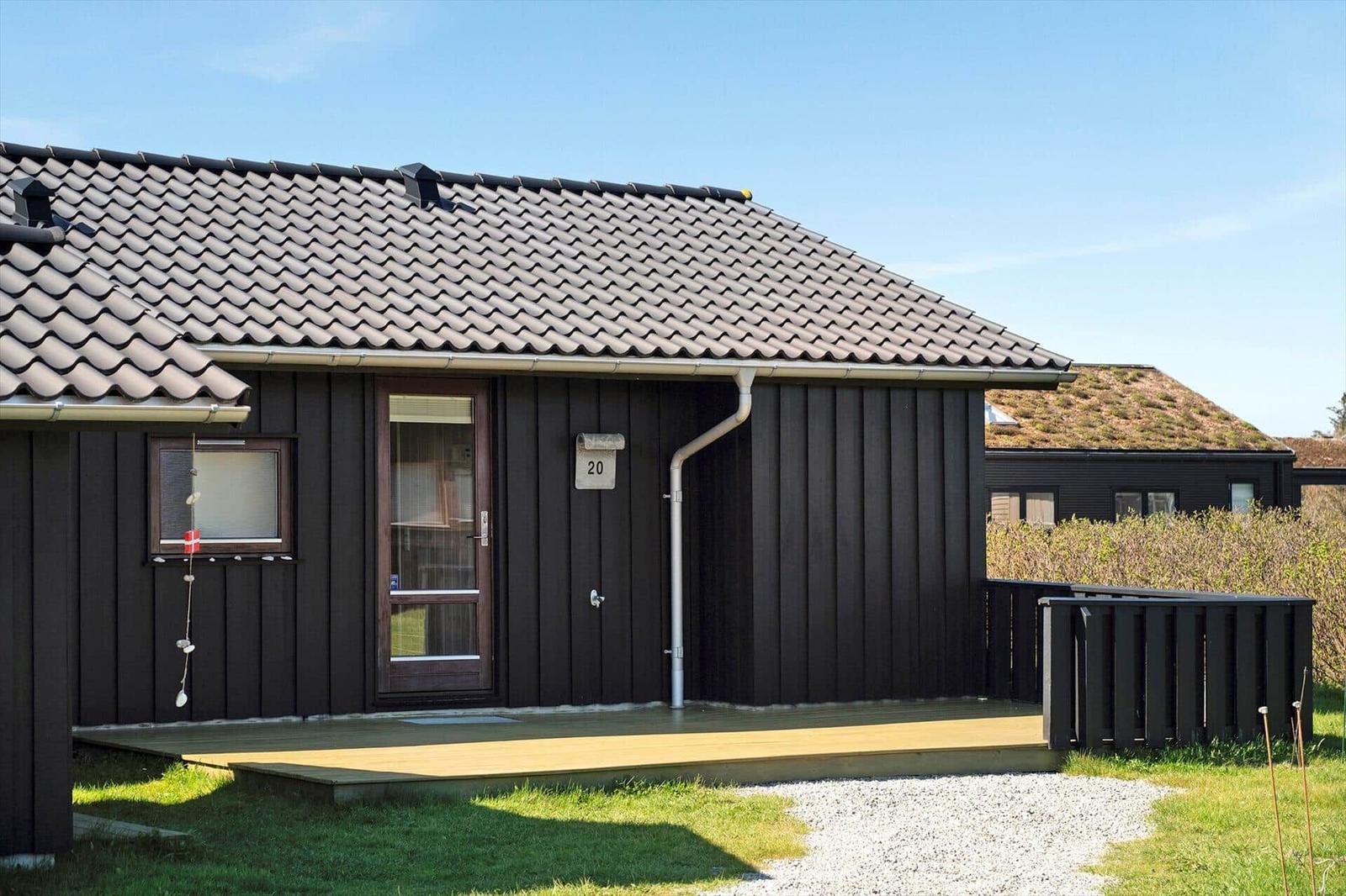 Ein Haus mit dunkler Holzfassade, Dach und Terrasse. Nummer 20 an der Tür.