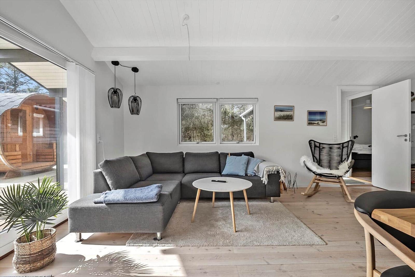 Wohnzimmer mit grauem Sofa, runden Tisch und Holzboden. Durchgang zur Schlafzimmer.