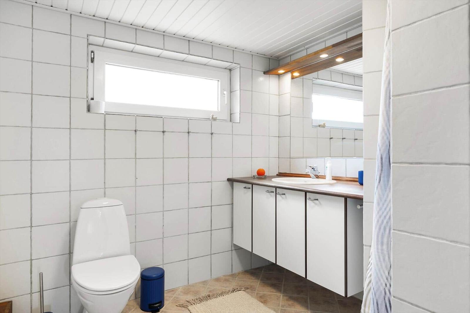 Bathroom with toilet, sink and shower. White tiles and wooden frame.