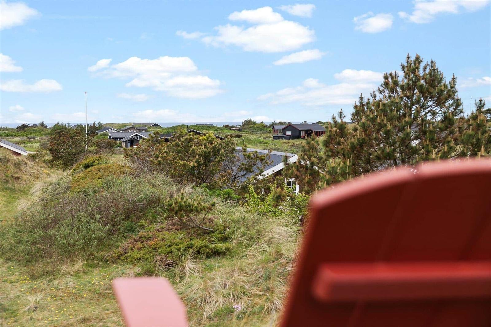Red chair with view of green dunes and vacation houses under blue sky.