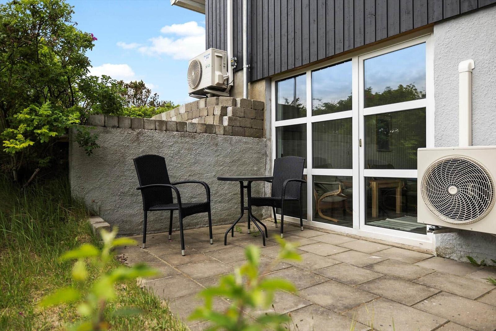 Outdoor area with table and two chairs next to glass doors and wall-mounted air conditioner.
