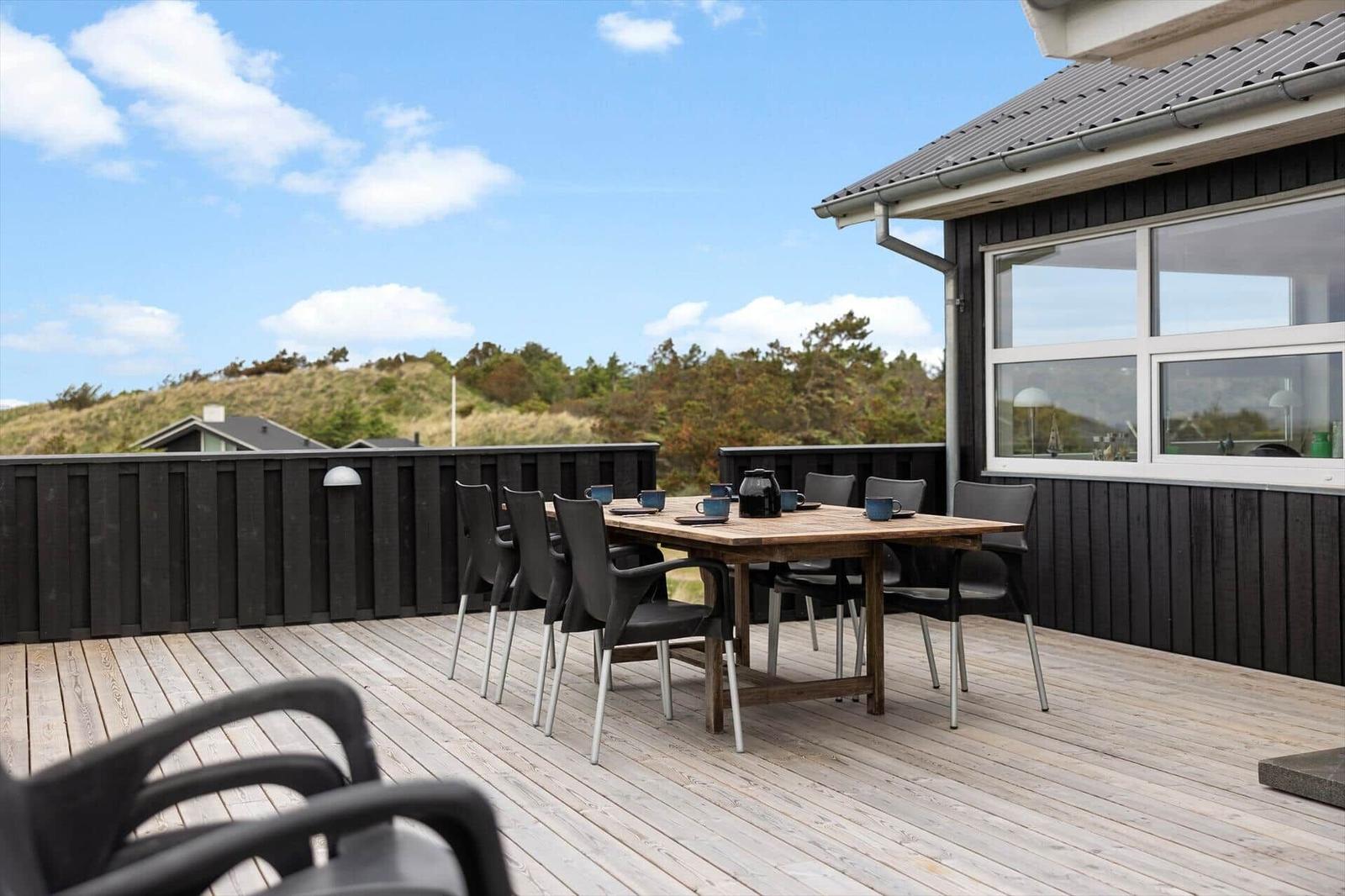 Deck with wooden table and chairs, view of hills and sky.